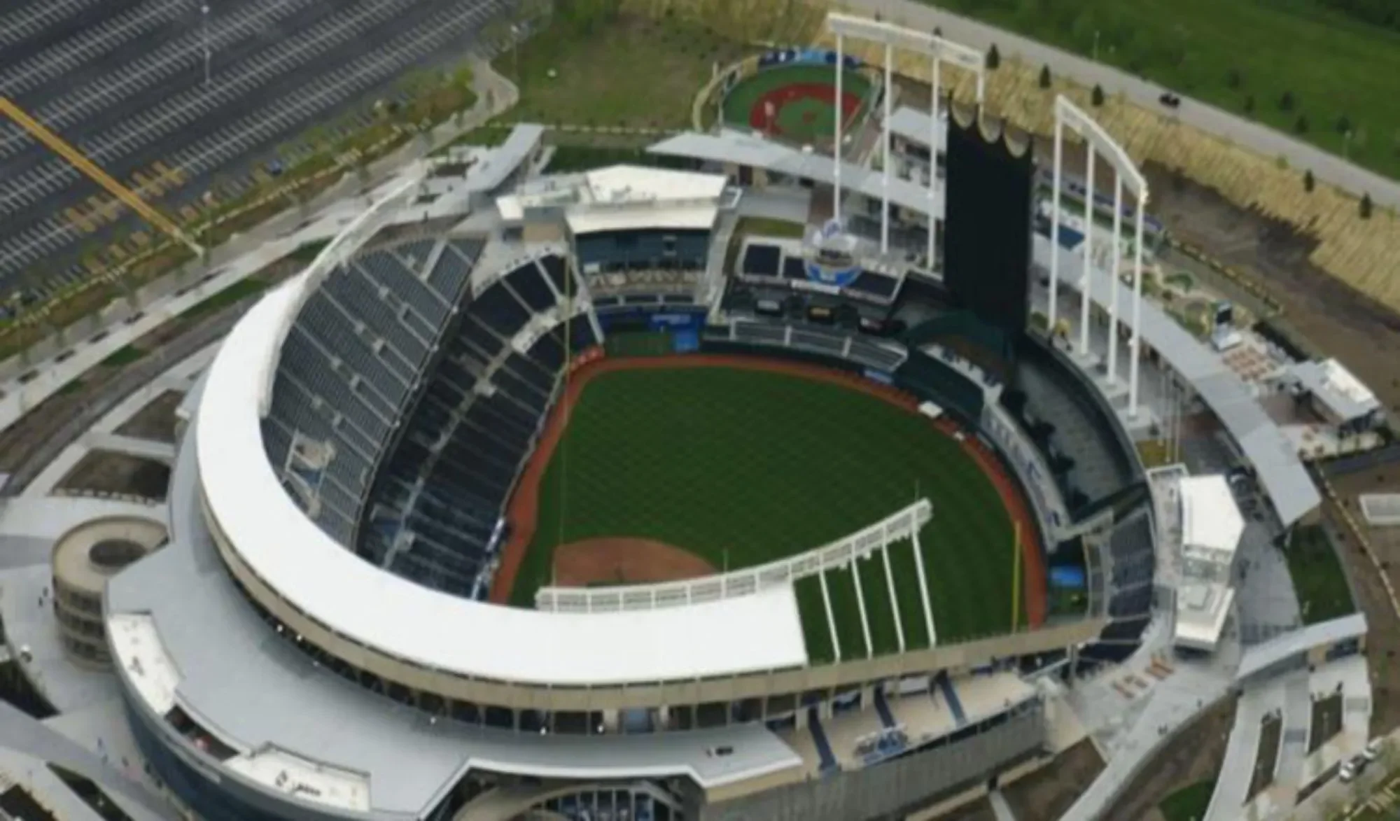 An aerial view of a baseball stadium with a green field, seating areas, and surrounding parking lots.