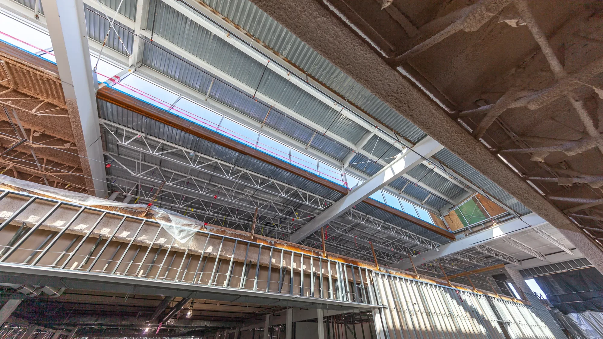 View of the interior of a building under construction with exposed steel beams, scaffolding, and partially finished walls and ceilings.