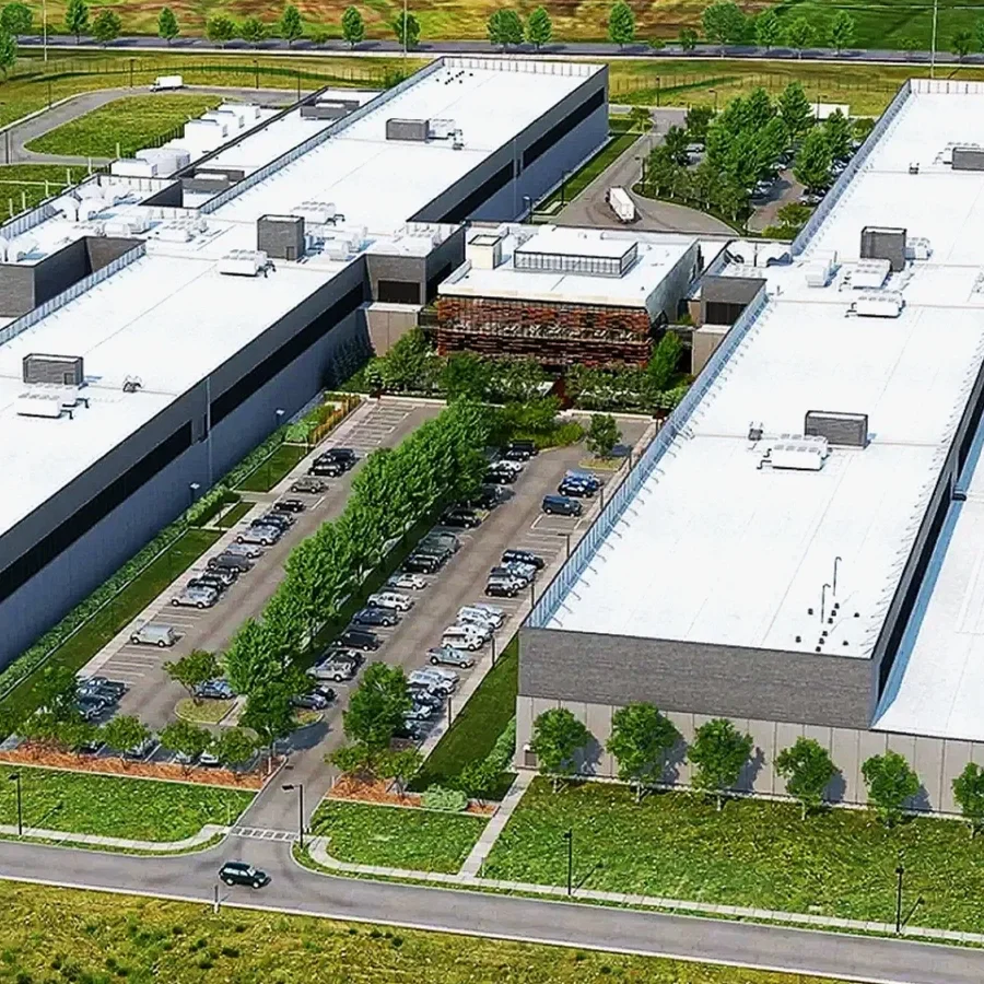 Aerial view of a large Data Center with a white roof, parking lots, trees, and green landscaping.