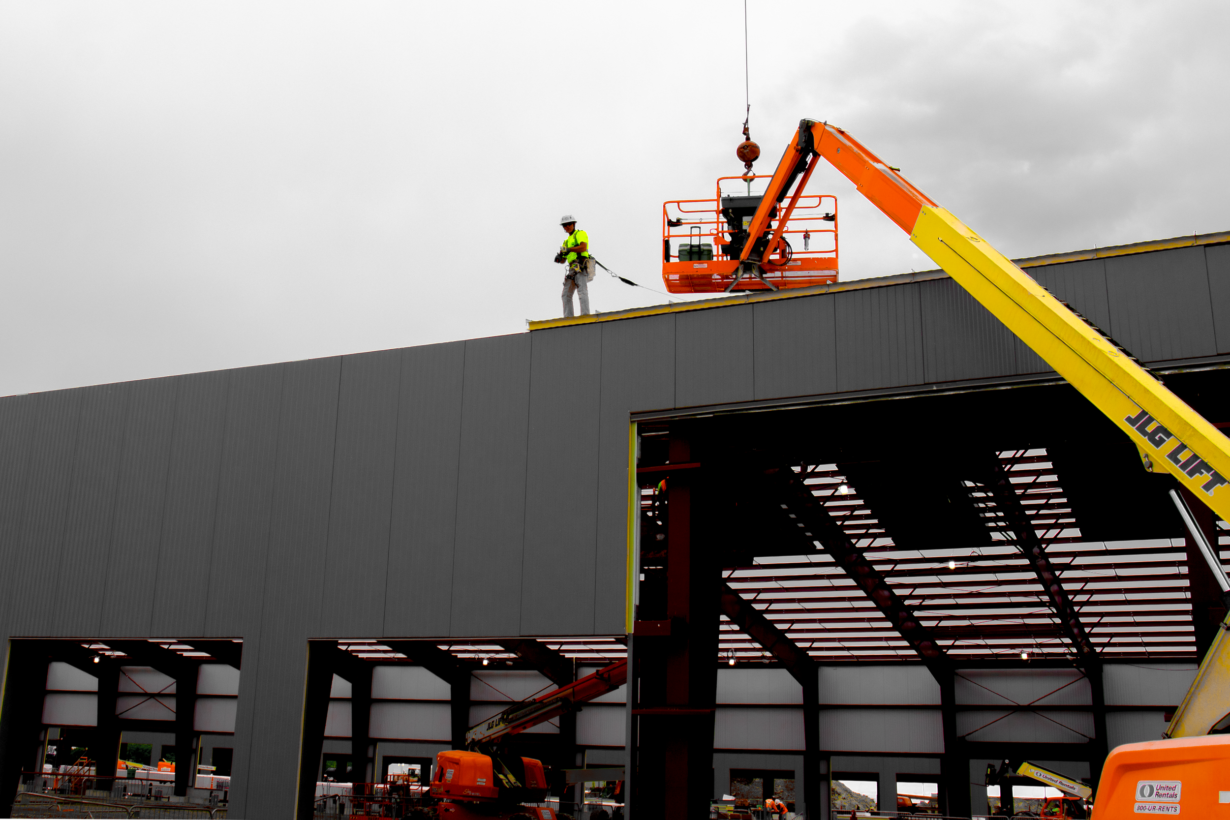 Construction workers on the roof of a building using an orange cherry picker lift during overcast weather.