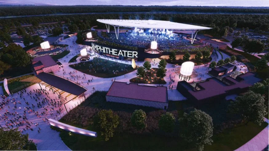 Nighttime aerial view of an amphitheater with a large stage, surrounded by trees and pathways, illuminated with purple lights, and a crowd of people gathering for a concert or event.