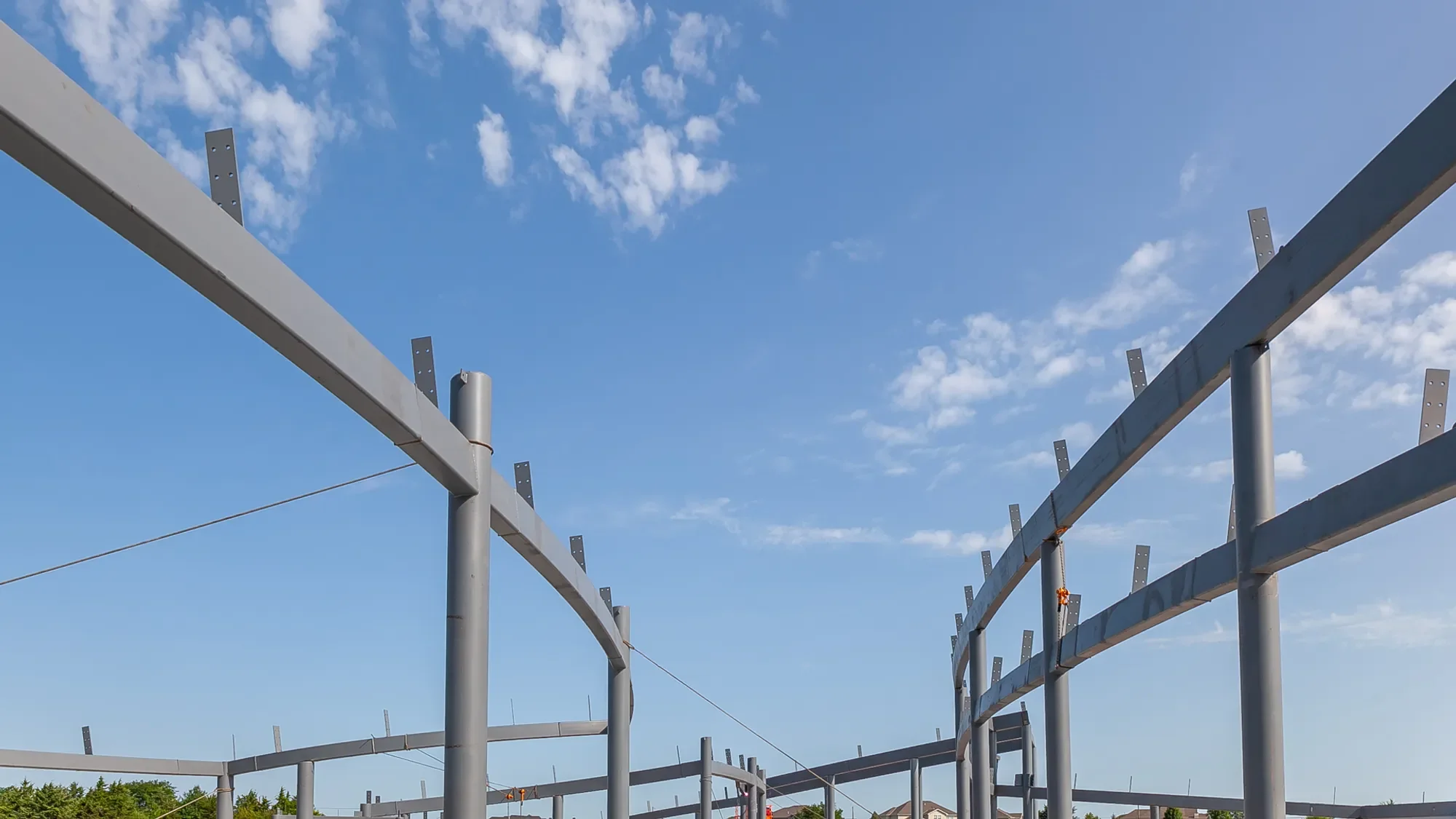 Steel framework of a building under construction against a background of partly cloudy blue sky.