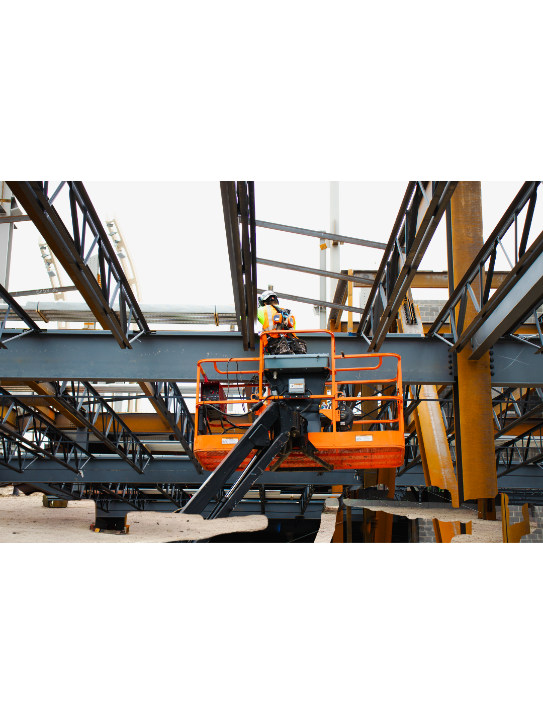 Construction worker in safety gear operating a lift at a building site with steel beams and framework.