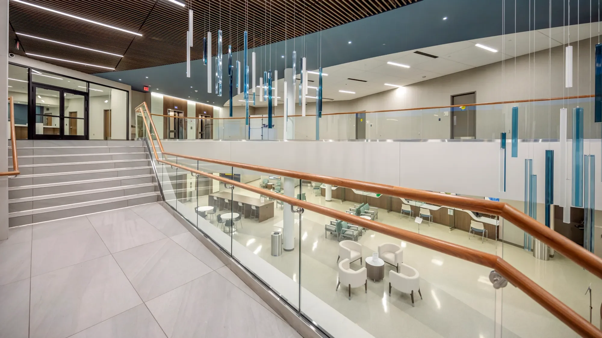 Modern multi-level interior with staircase, glass railings, hanging blue and white decorative elements, and seating area below.