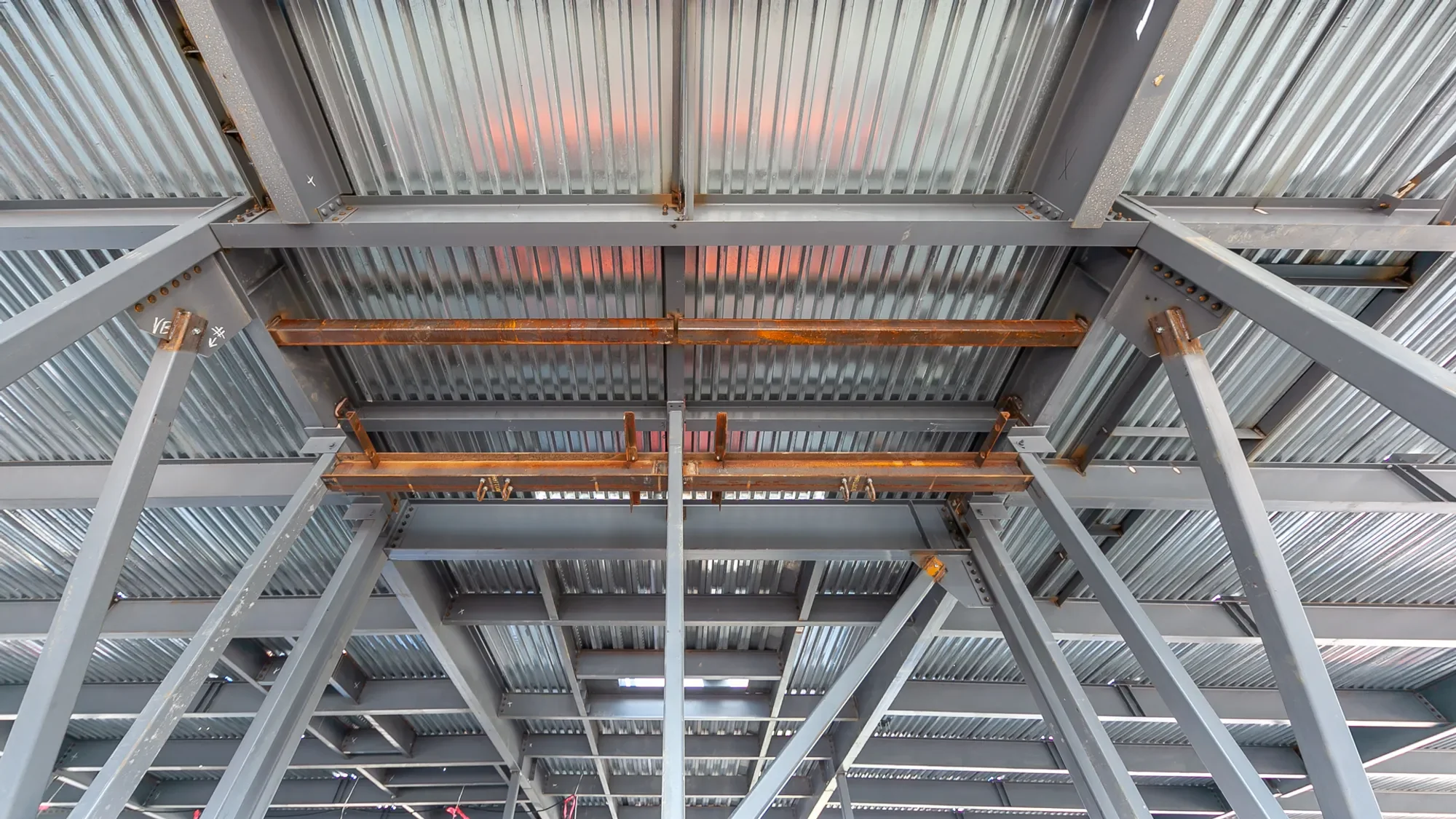 Under construction steel framework with metal roofing panels, showing rusted and new metal beams and supports inside a building under construction.