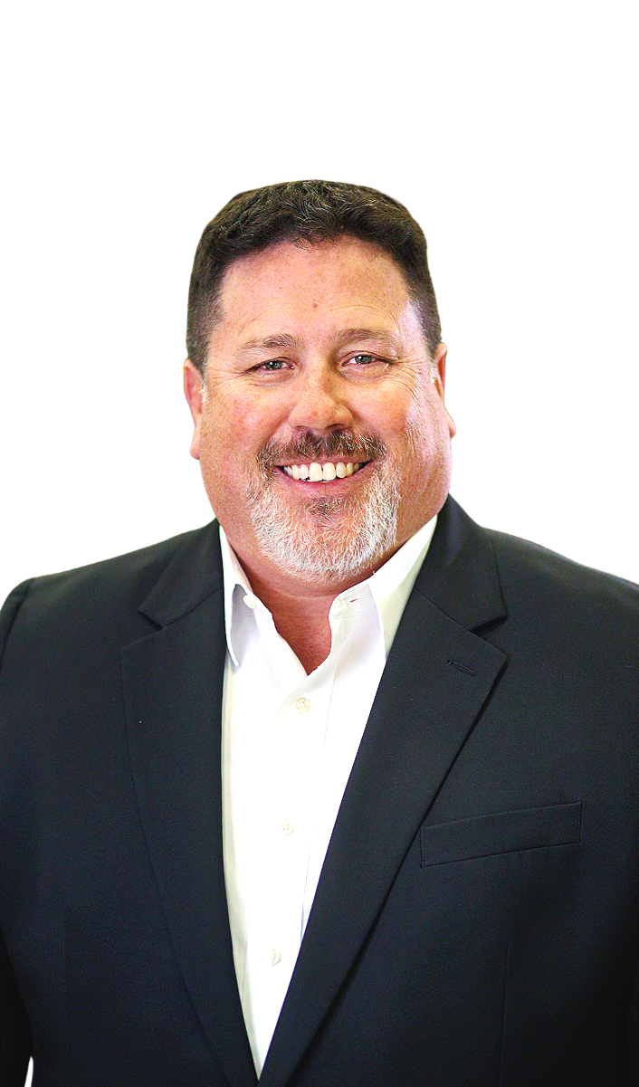 A smiling middle-aged man with dark hair, facial hair, wearing a black suit jacket and a white dress shirt, against a black background.
