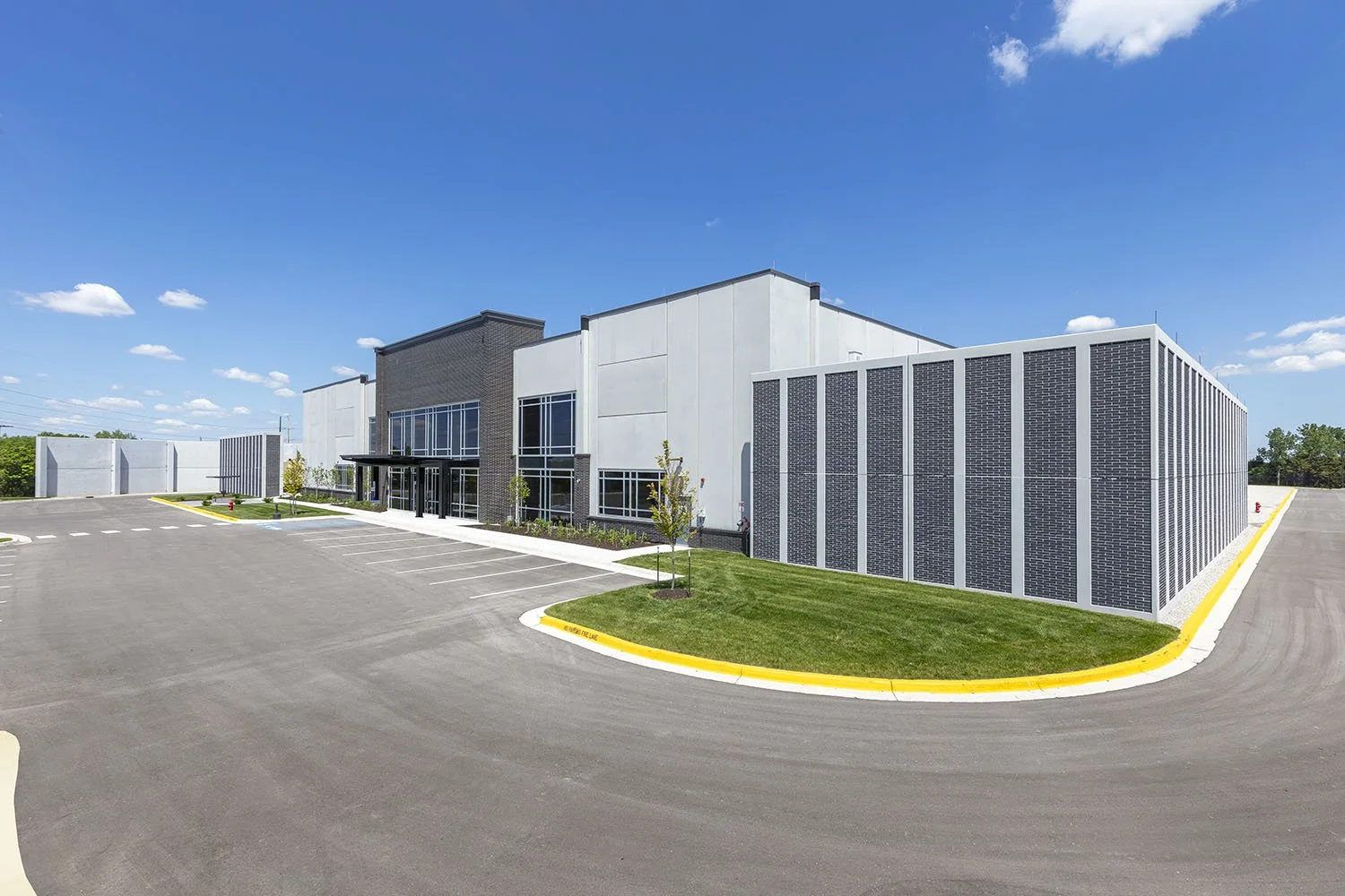 Modern commercial building with large parking lot, blue sky, and small trees.