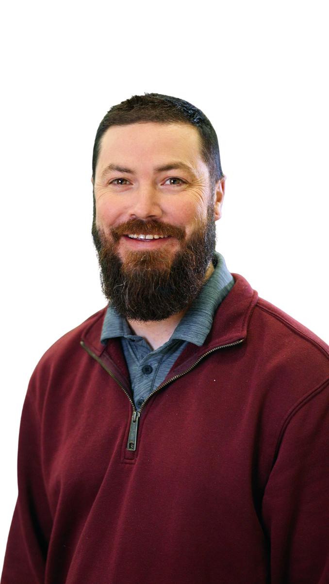 A smiling man with a beard and short dark hair, wearing a burgundy zip-up jacket over a gray collared shirt, against a black background.