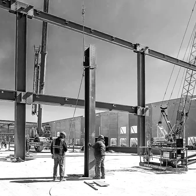 Construction workers assembling steel framework for a building with cranes and construction equipment in the background.