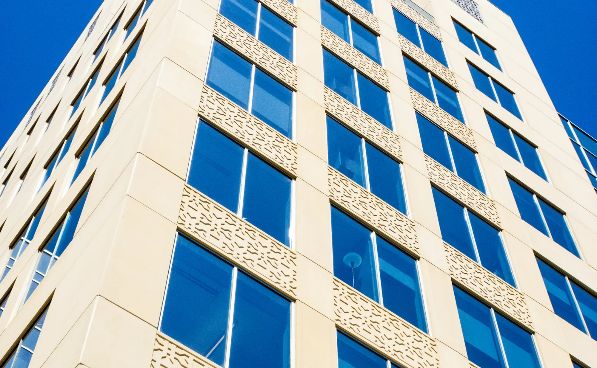 A modern multi-story building with blue glass windows and beige decorative panels against a clear blue sky.