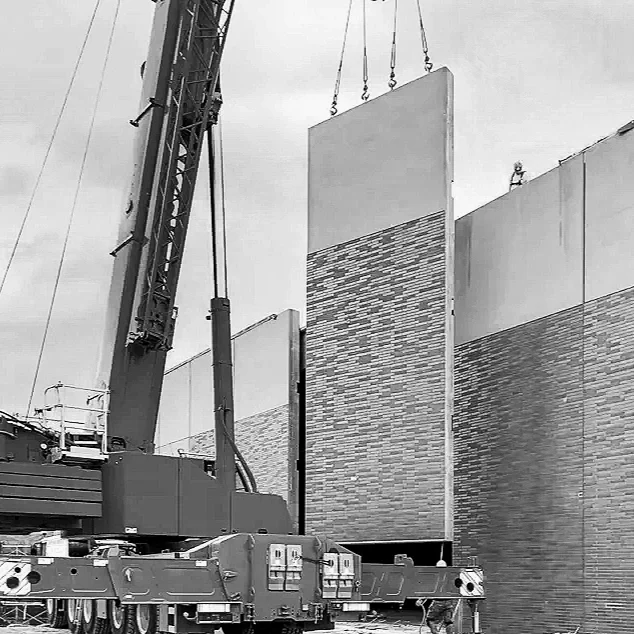 A crane installing a large decorative wall panel featuring brick pattern sections on a building under construction or renovation.