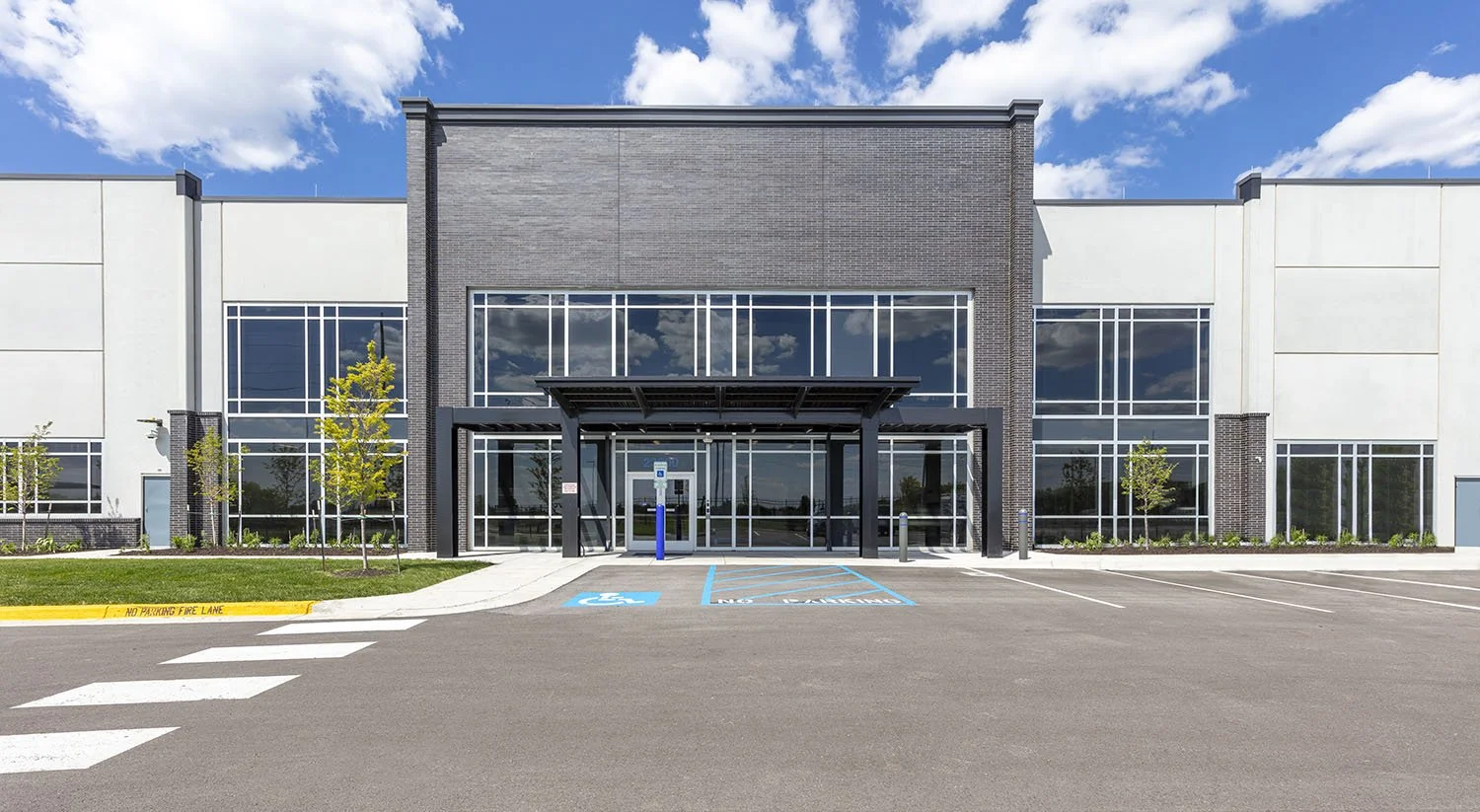 Modern commercial building with large glass windows, a covered entrance, and clearly marked accessible parking spots in the front, under a partly cloudy sky.