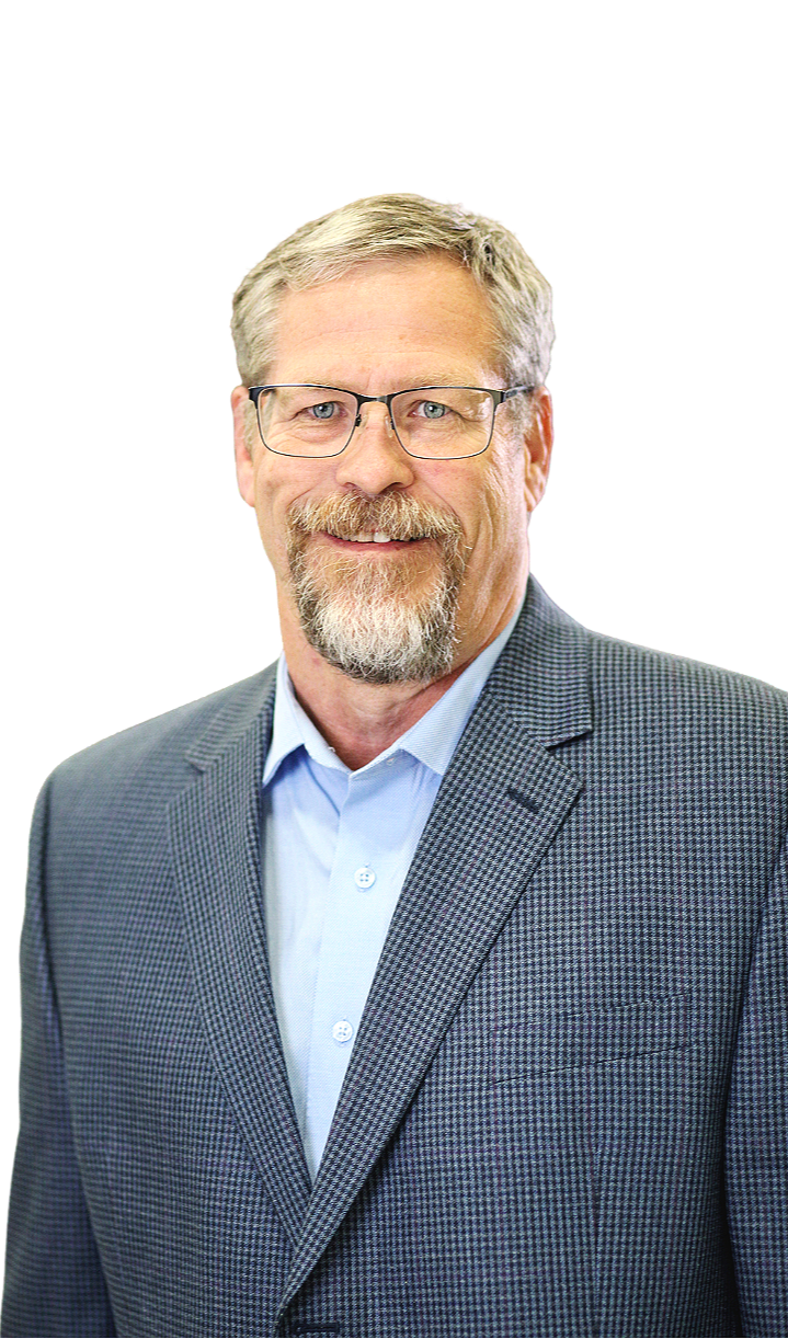 A middle-aged man with gray hair, a beard, and glasses, wearing a gray checkered suit jacket and a light blue dress shirt, smiling at the camera.