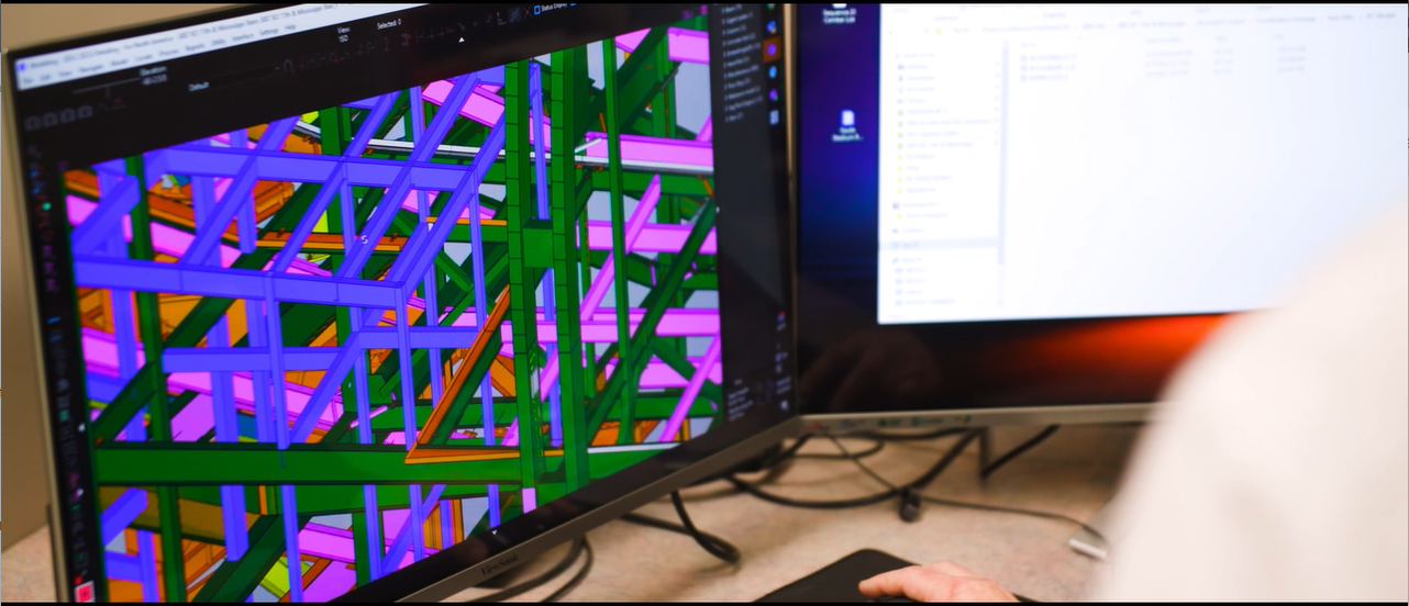 Computer monitors displaying a 3D structural model with multicolored interconnected beams.