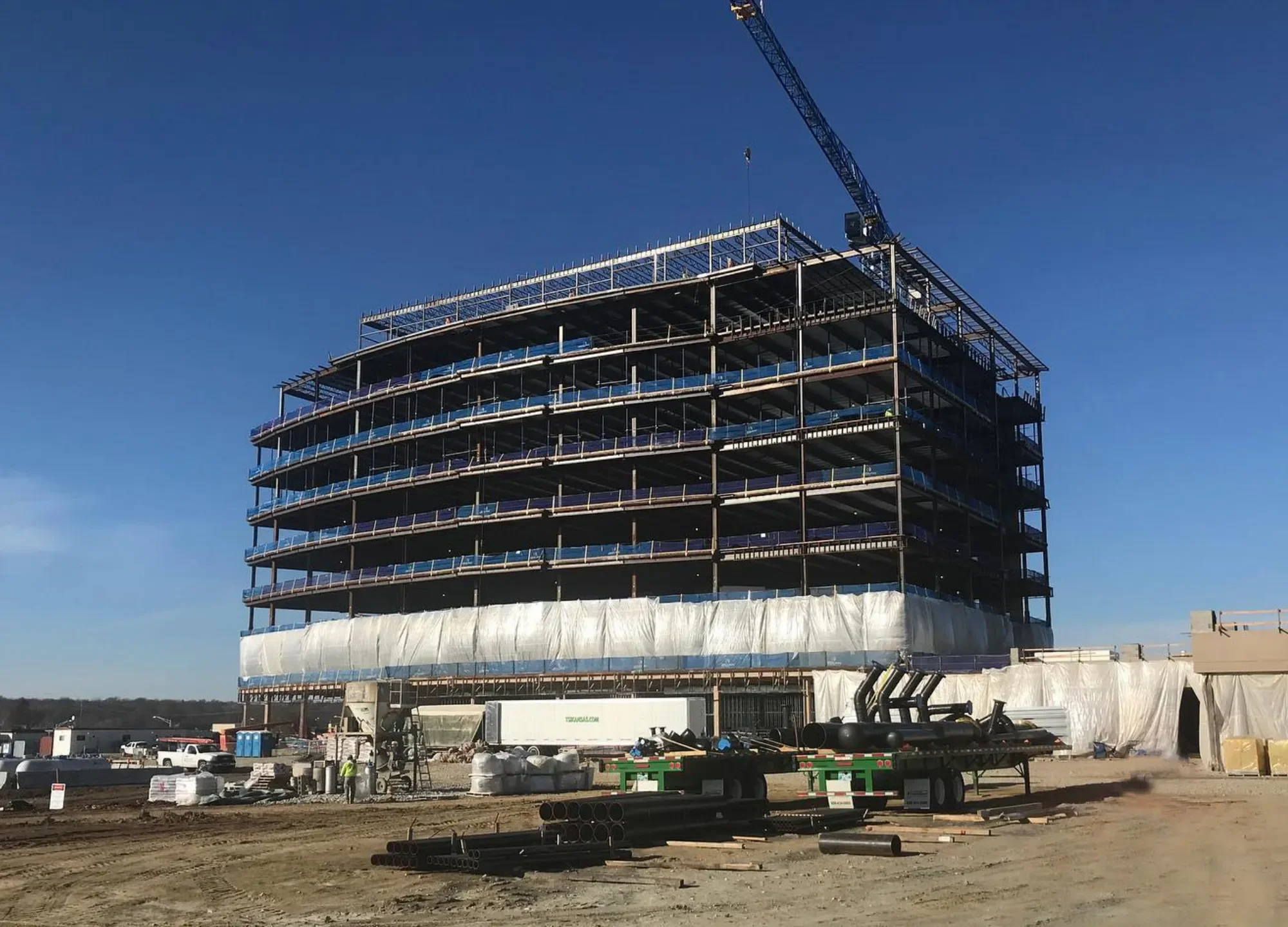 Under construction multi-story building with scaffolding and a crane at the top, set against a clear blue sky.
