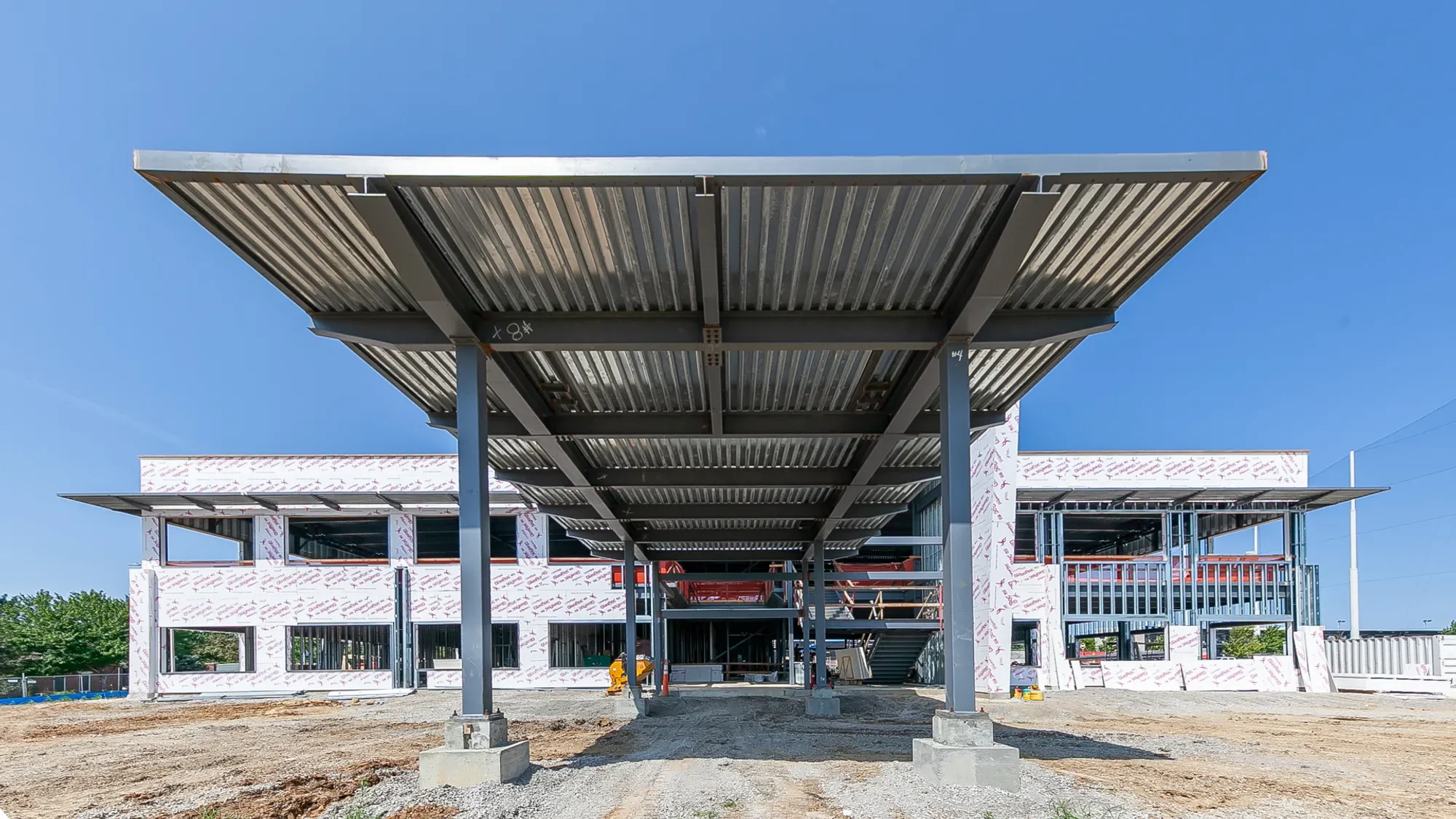 Under construction building with a metal awning supported by steel columns, partially finished building with windows and exterior walls.