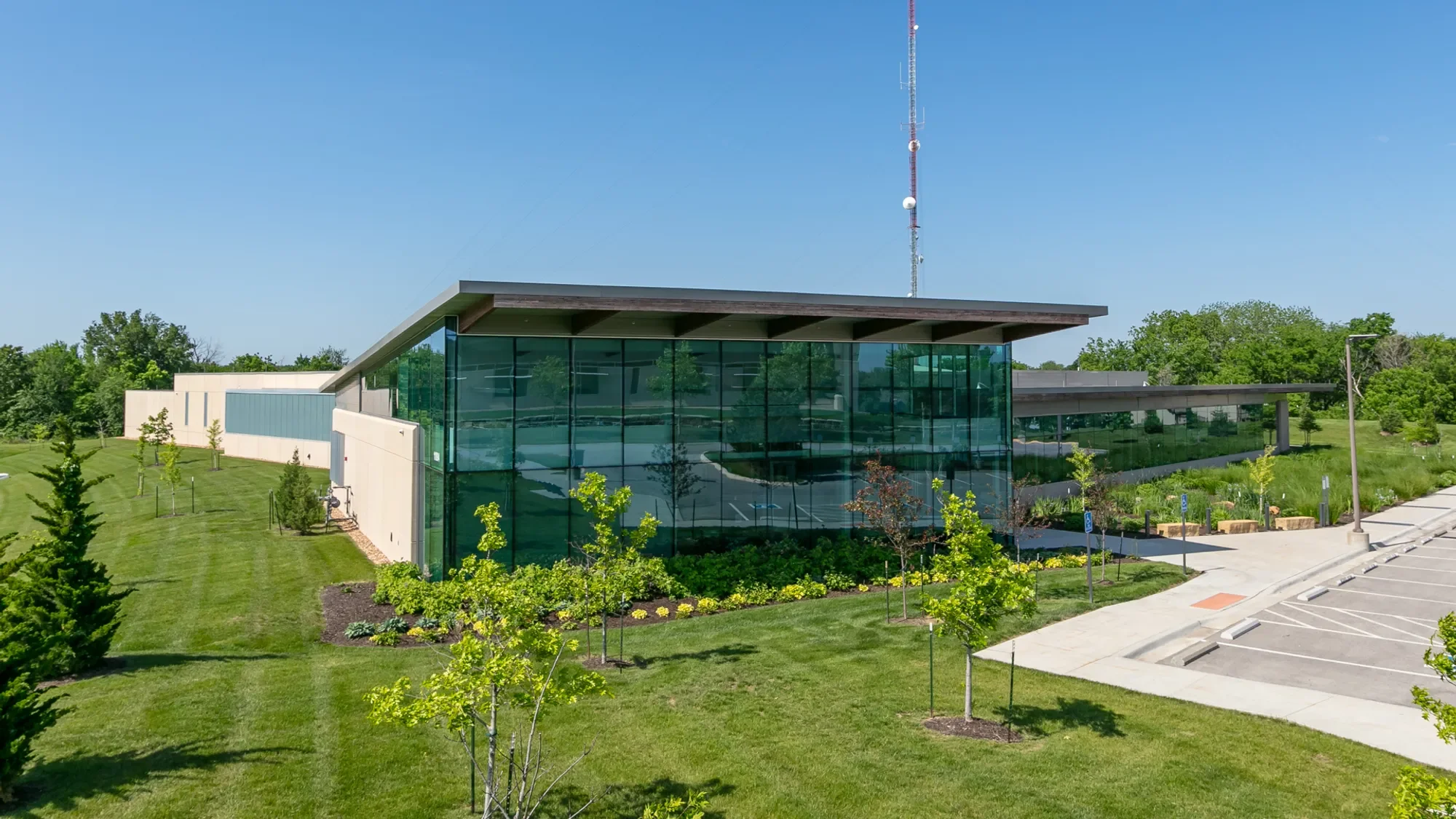 Modern building with large glass windows, surrounded by green trees and grass, with a clear blue sky in the background.