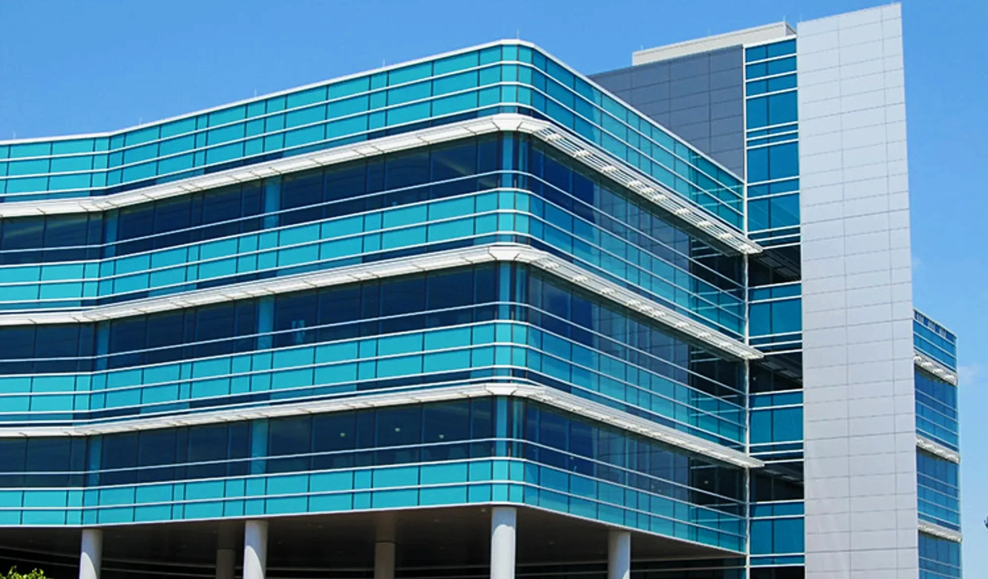 Modern multi-story glass building with curved architecture and blue sky background.