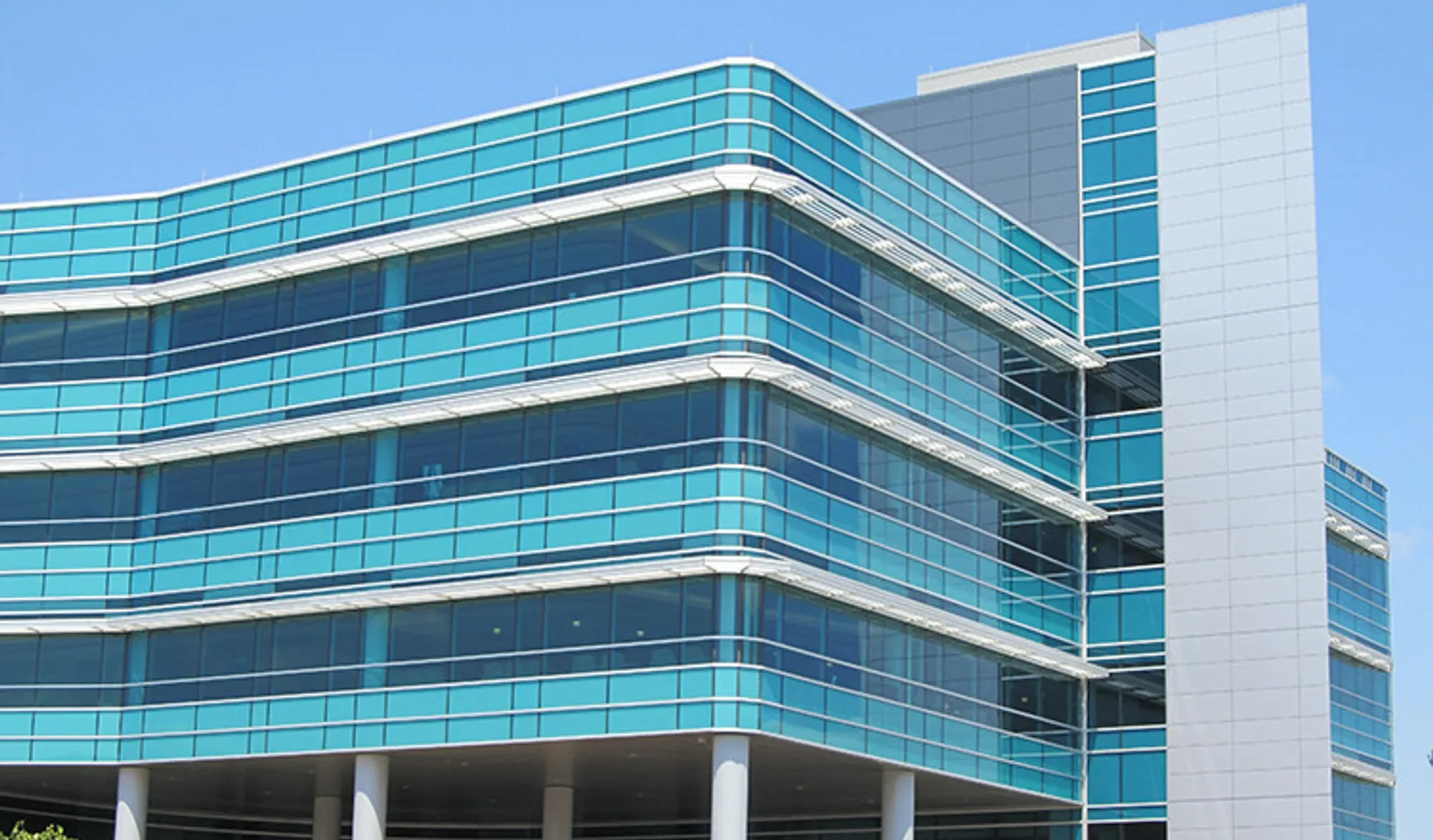 Modern glass office building with curved and rectangular sections against a clear blue sky.