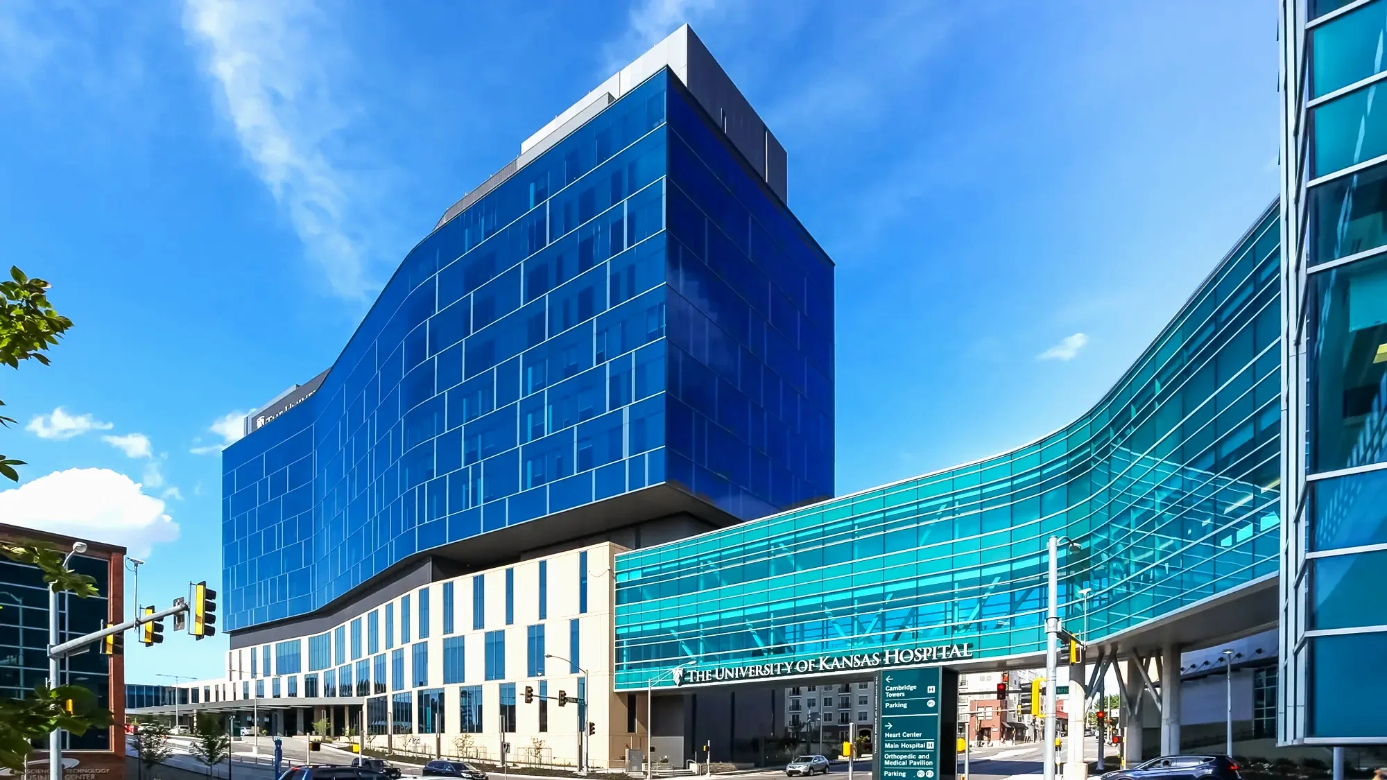 Modern blue glass building at the University of Kansas Hospital, with clear sky and traffic lights in the foreground.