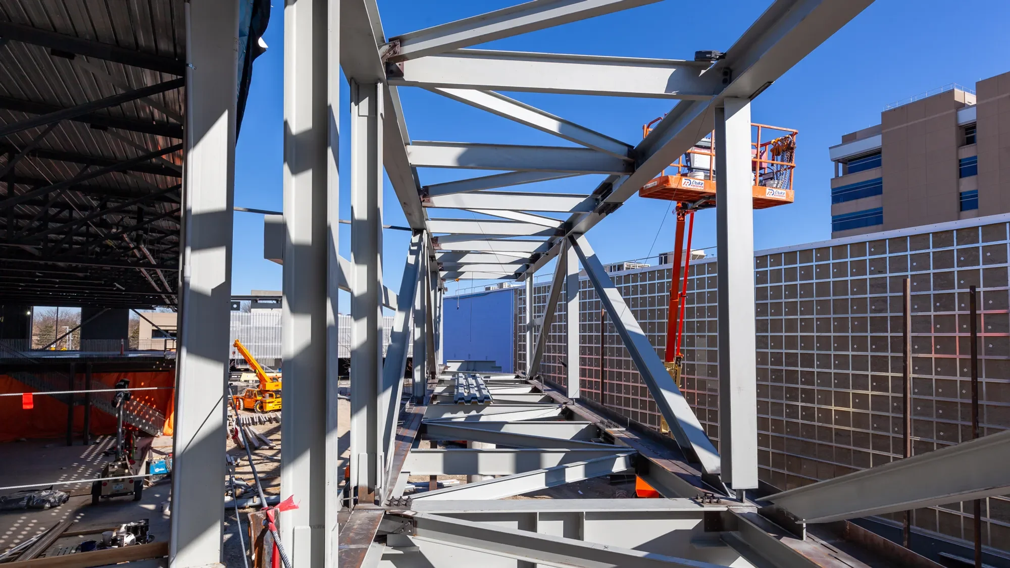 Construction site with steel framework and a red scissor lift on a clear day with blue sky.