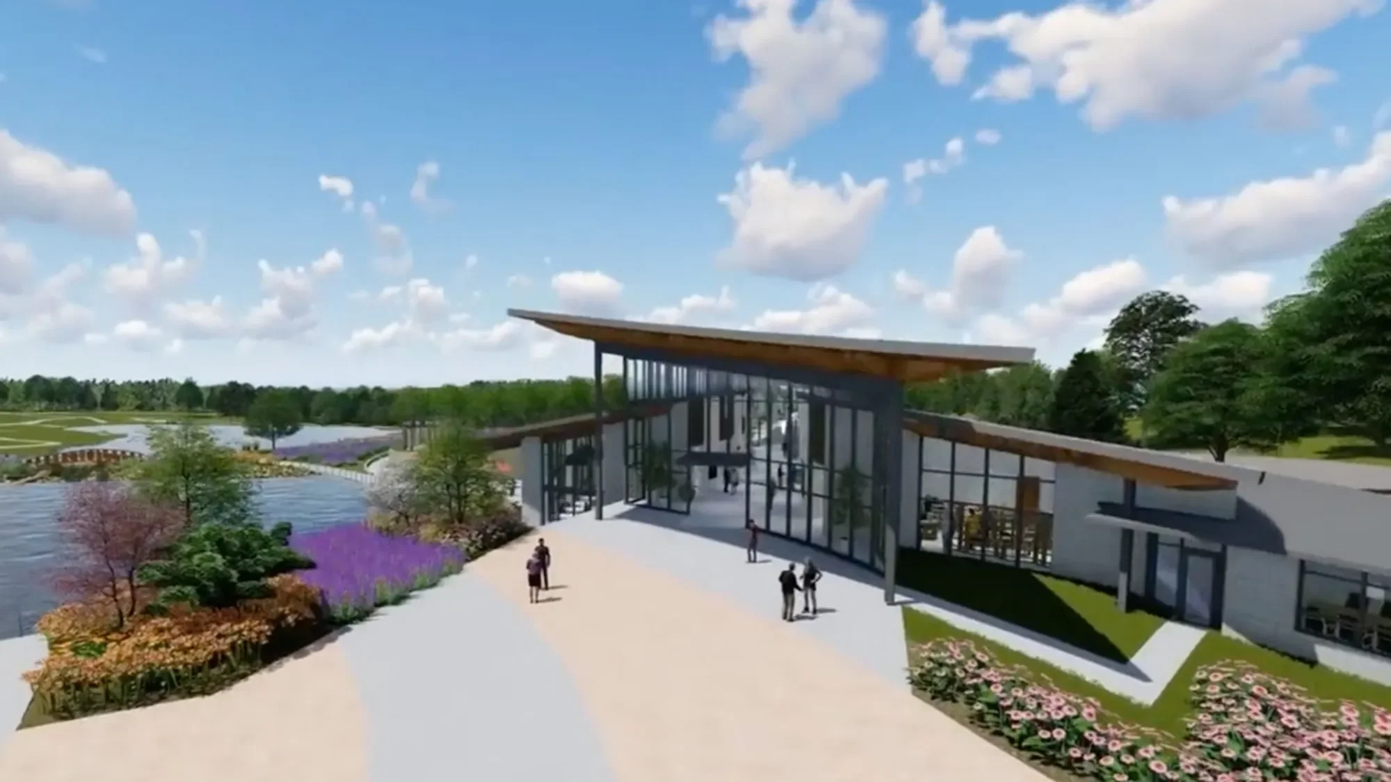 A modern building with large glass windows and a slanted wooden roof, surrounded by landscaped gardens and water features, with people walking on a paved pathway outside. In the background, there are green trees and a blue sky with scattered clouds.