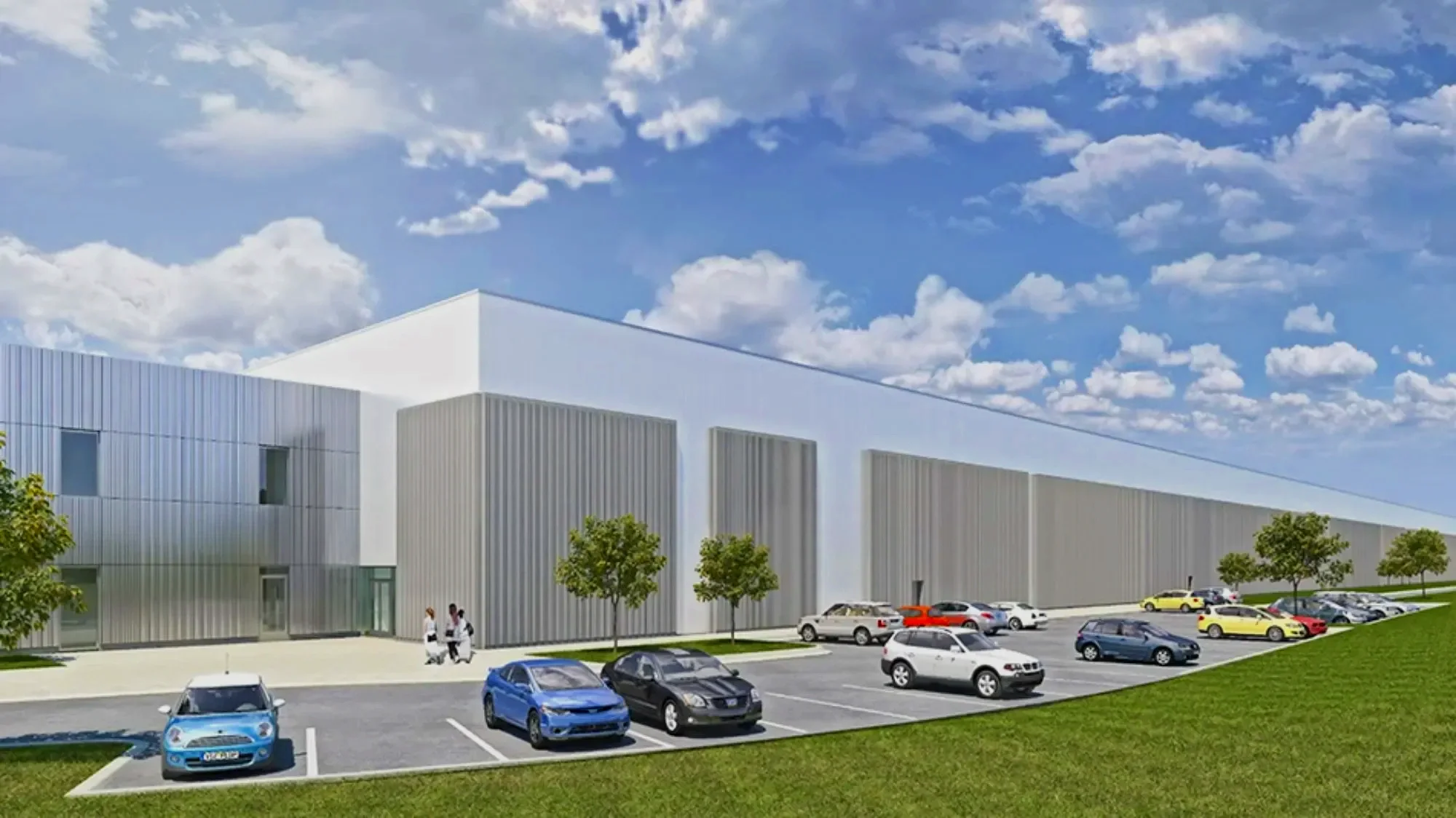 Modern building with white and gray exterior, surrounded by trees and a parking lot filled with cars, under a partly cloudy blue sky.