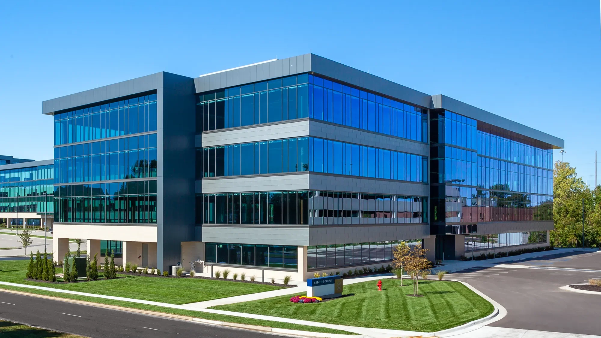 Modern office building with large glass windows and landscaped surroundings under a clear blue sky.