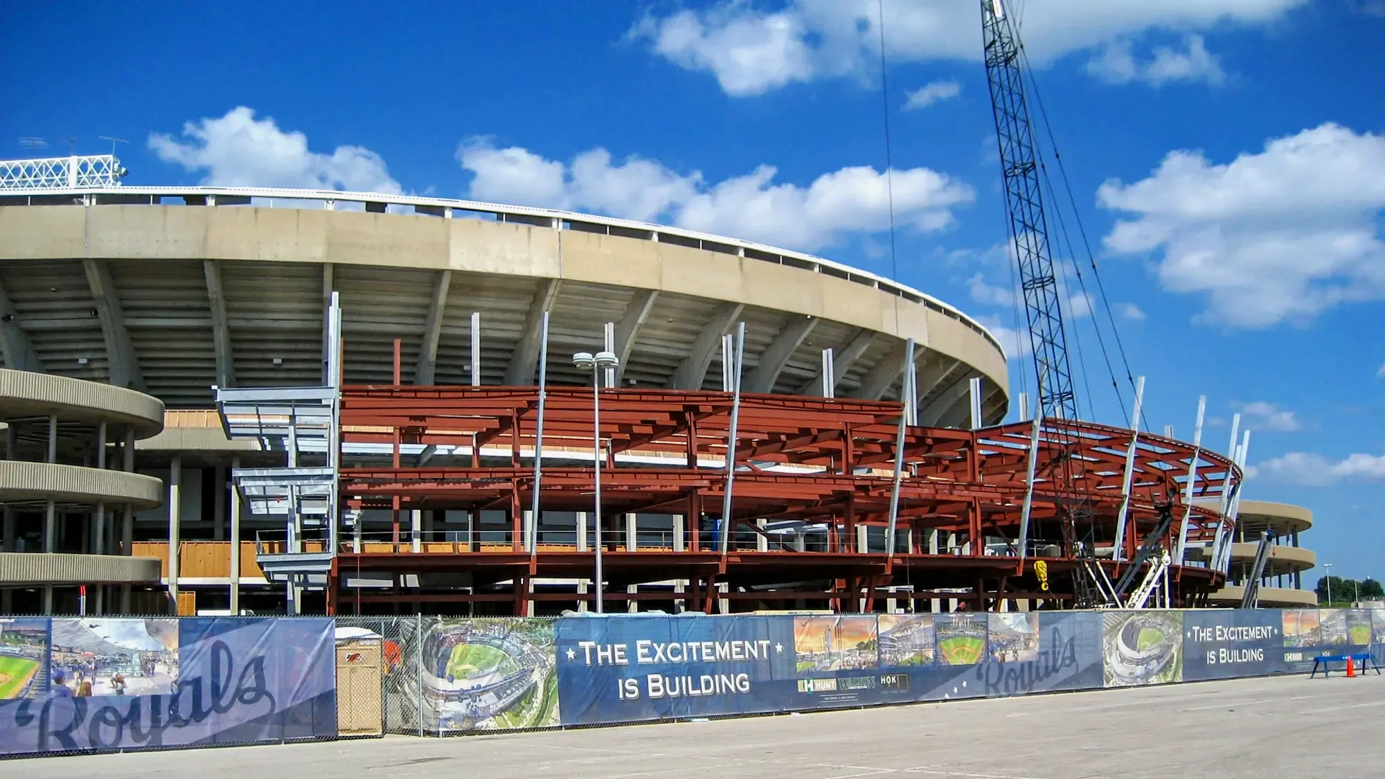 Under construction stadium with cranes and a banner saying 'The excitement is building'