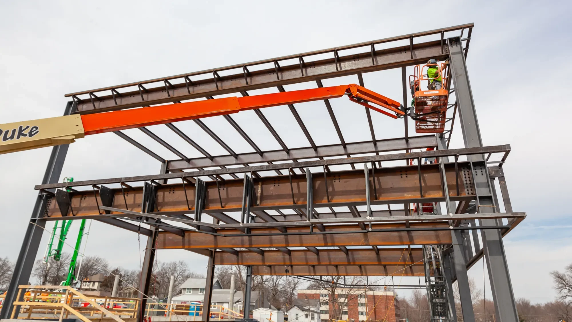 Construction worker standing in an elevated orange lift working on a metal framework of a building under construction.