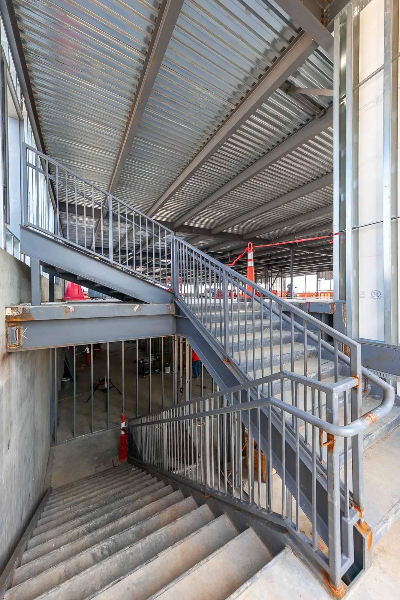 Construction site with metal stairs and railings inside a building under construction, with orange safety cones and scaffolding.