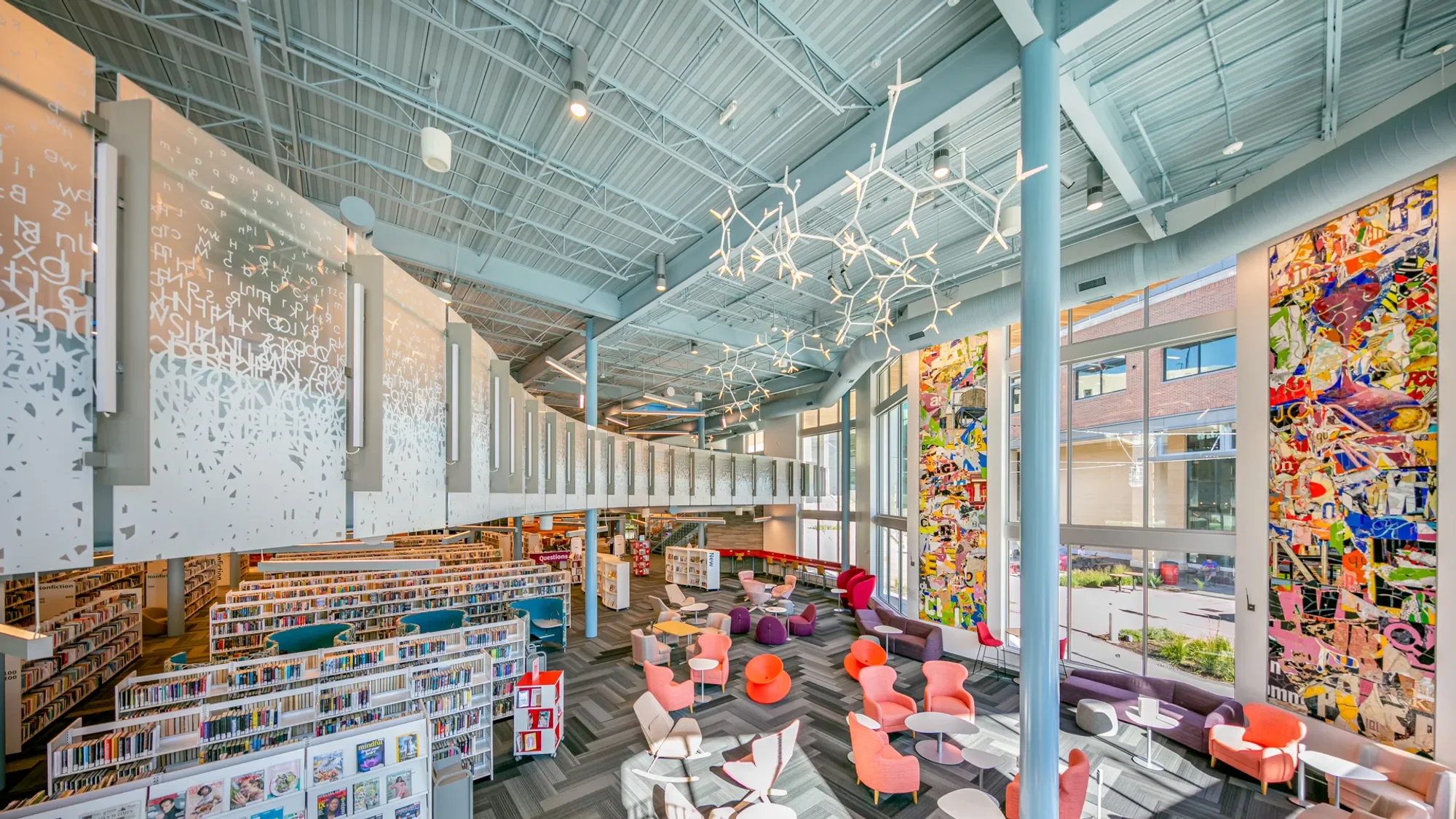 Interior of a modern library with large windows, colorful chairs, bookshelves, and contemporary lighting fixtures.