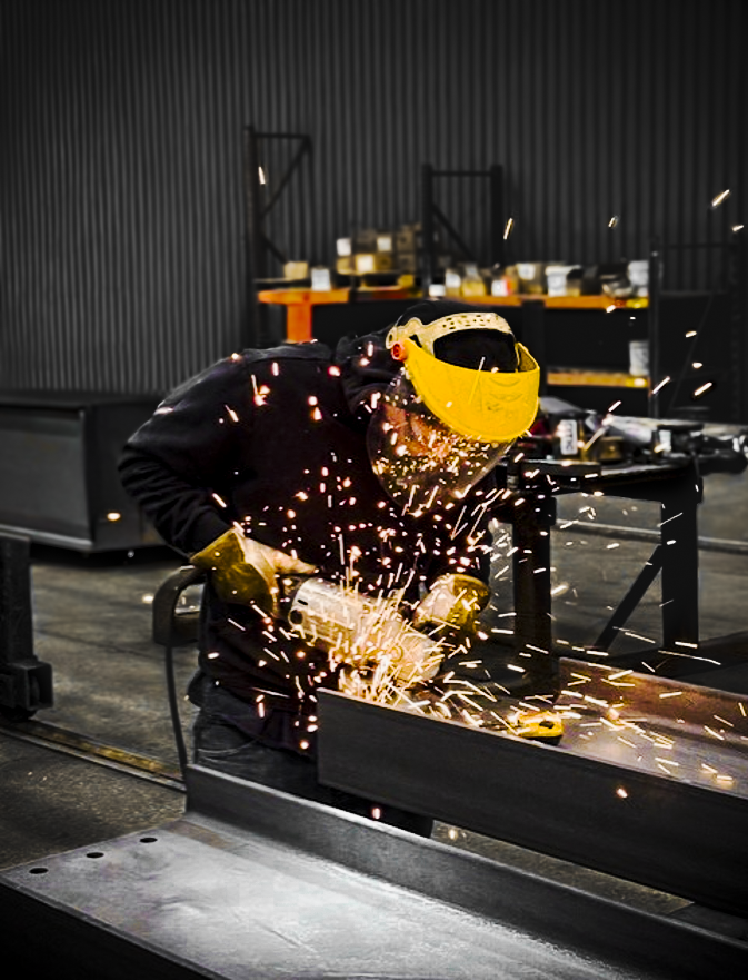 A worker wearing safety gear welding metal, with sparks flying in a workshop.