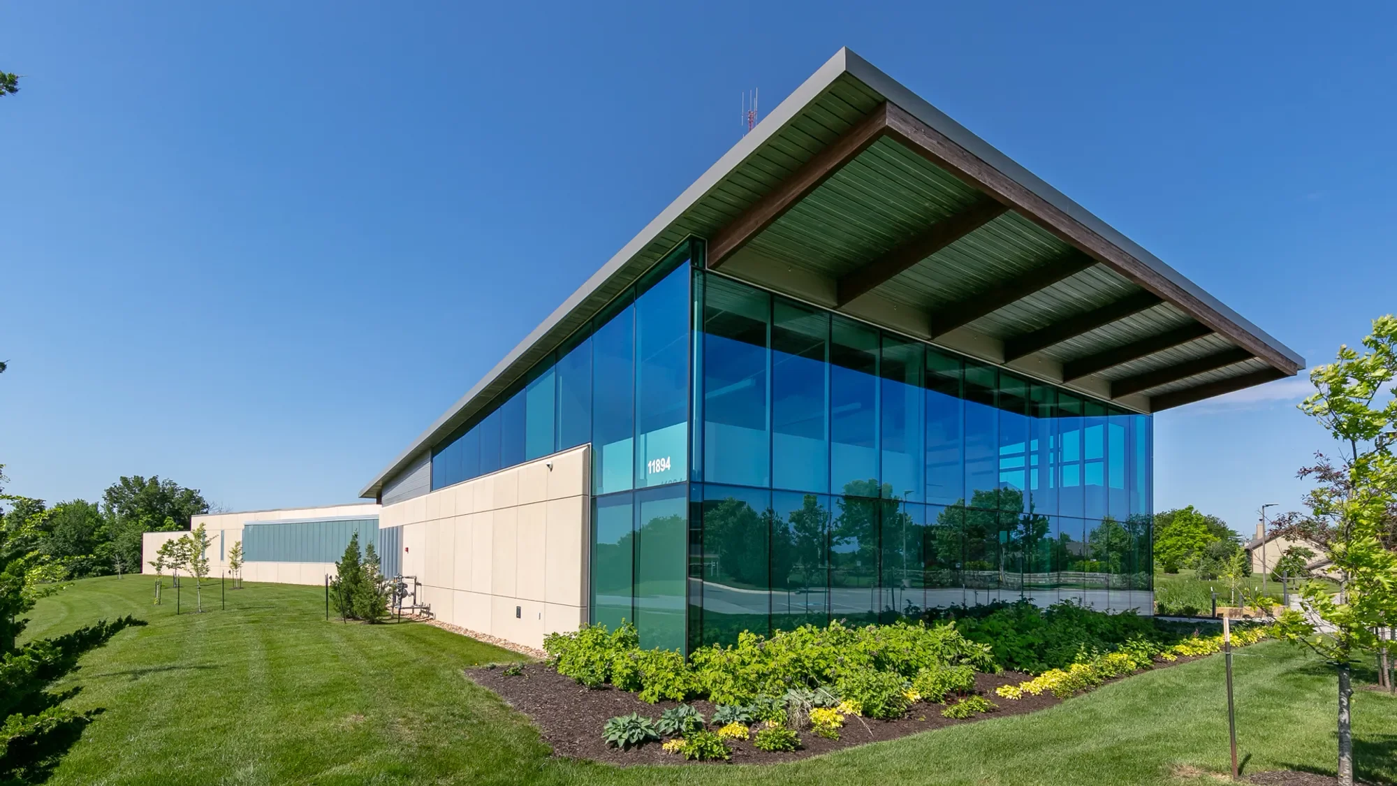 Modern commercial building with large glass windows, surrounded by well-maintained green lawn and landscaping, under a clear blue sky.