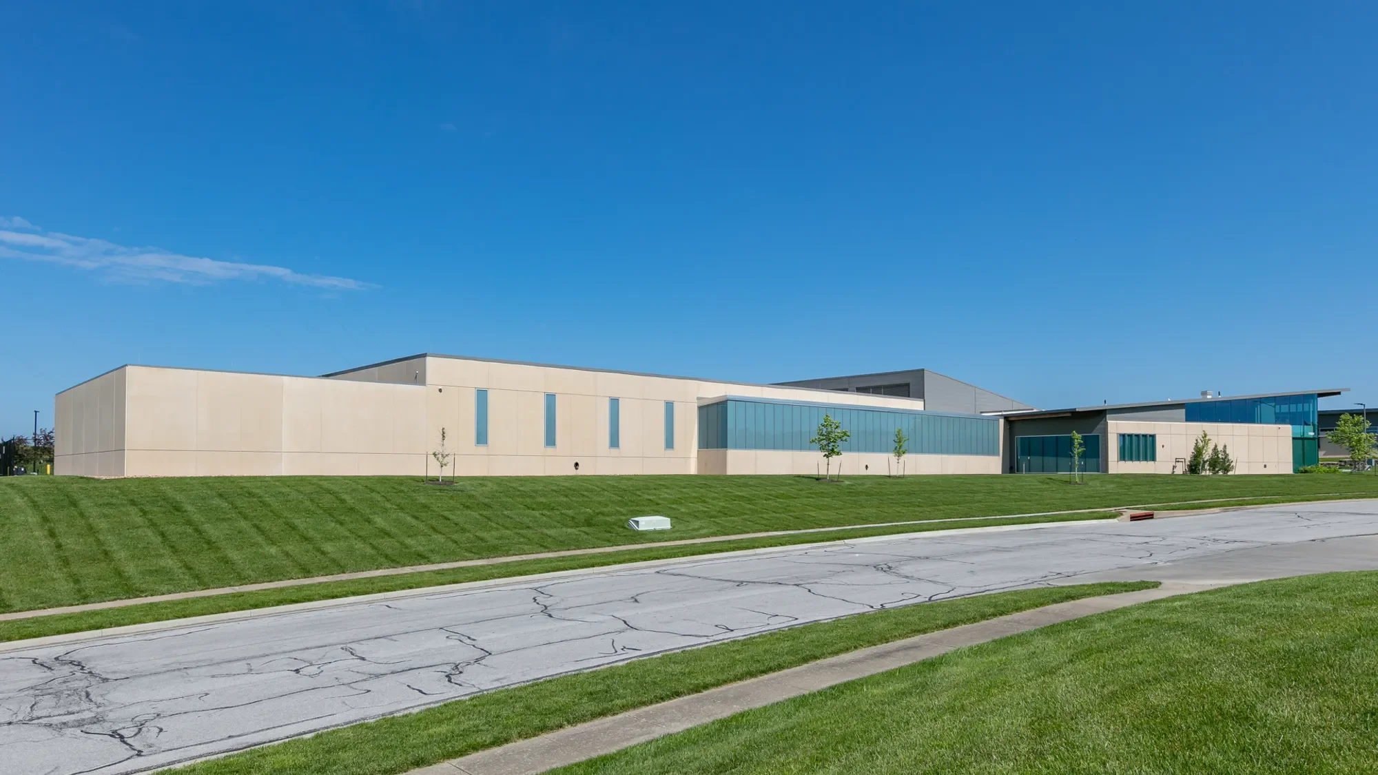 Modern building with beige and glass exterior, surrounded by green lawn and small trees, under a clear blue sky.