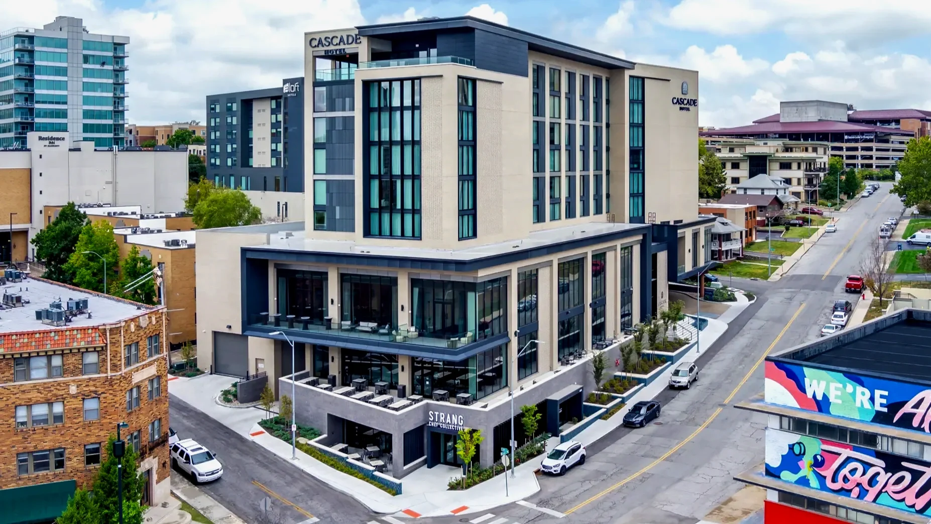 A modern multi-story hotel called Cascade Hotel in an urban area, with a restaurant named STRANG Chef Collectiv on the ground floor, tall glass windows, and a city street with parked cars and nearby buildings.
