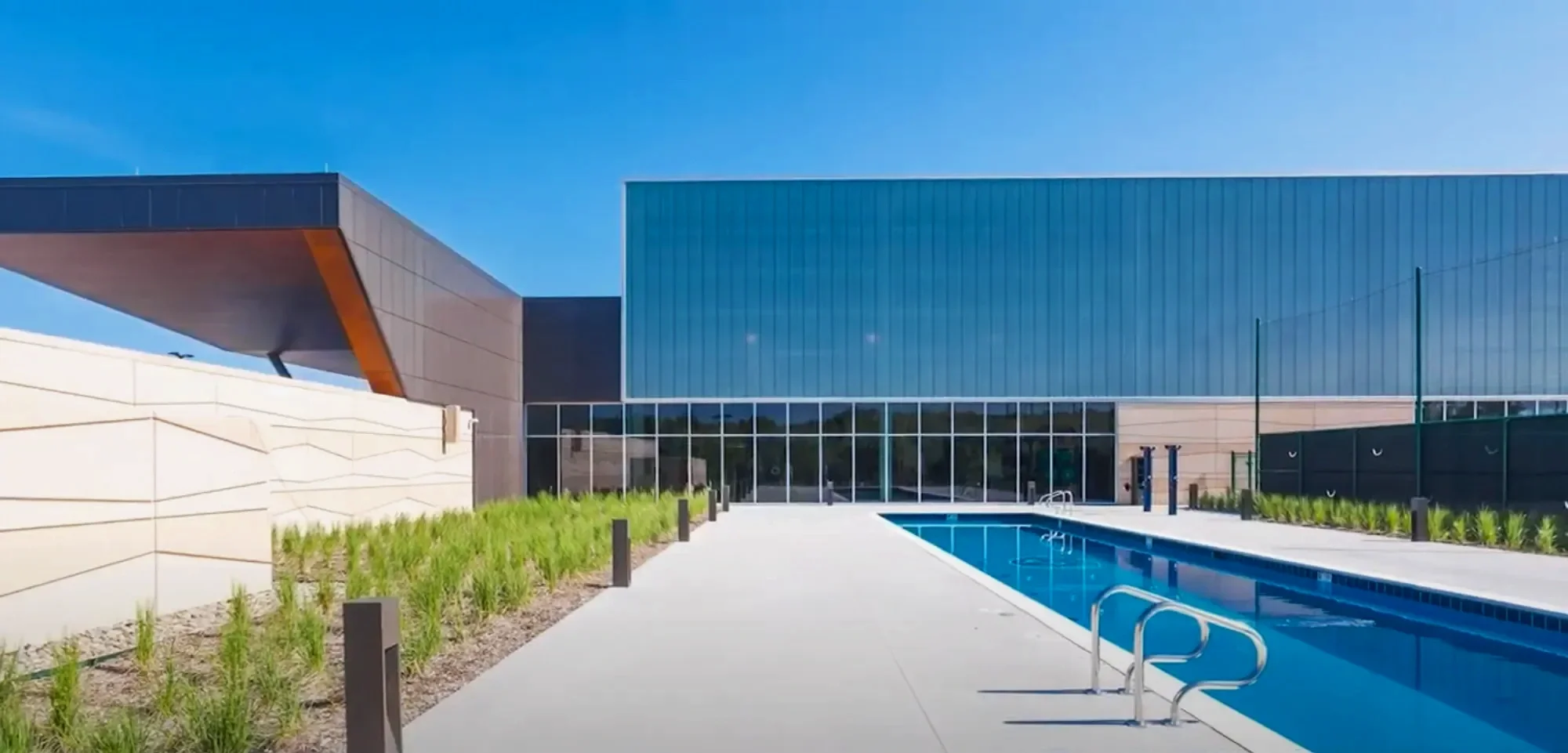 Modern building with glass facade and outdoor swimming pool under a clear blue sky.