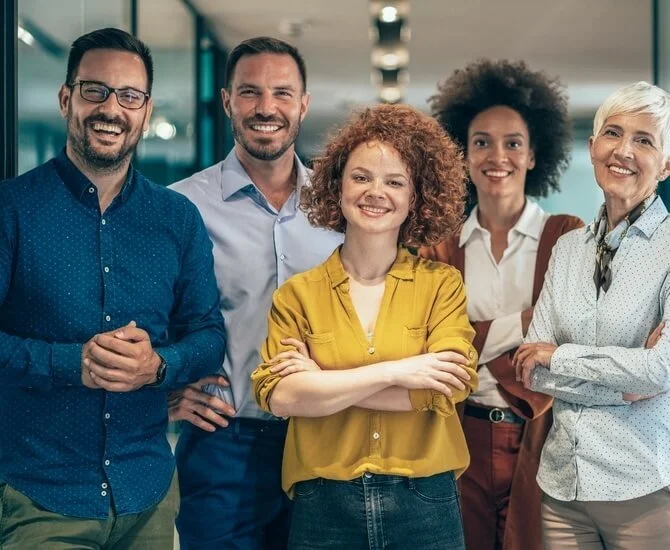 Fünf Menschen von unterschiedlichen ethnischen Hintergründen stehen zusammen in einem Büro, lachen und wirken glücklich.