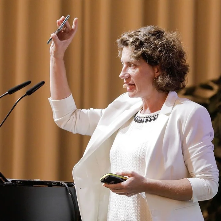 Andrea Belliger hält in der Hand ein Handy, während sie auf einer Bühne spricht oder präsentiert.