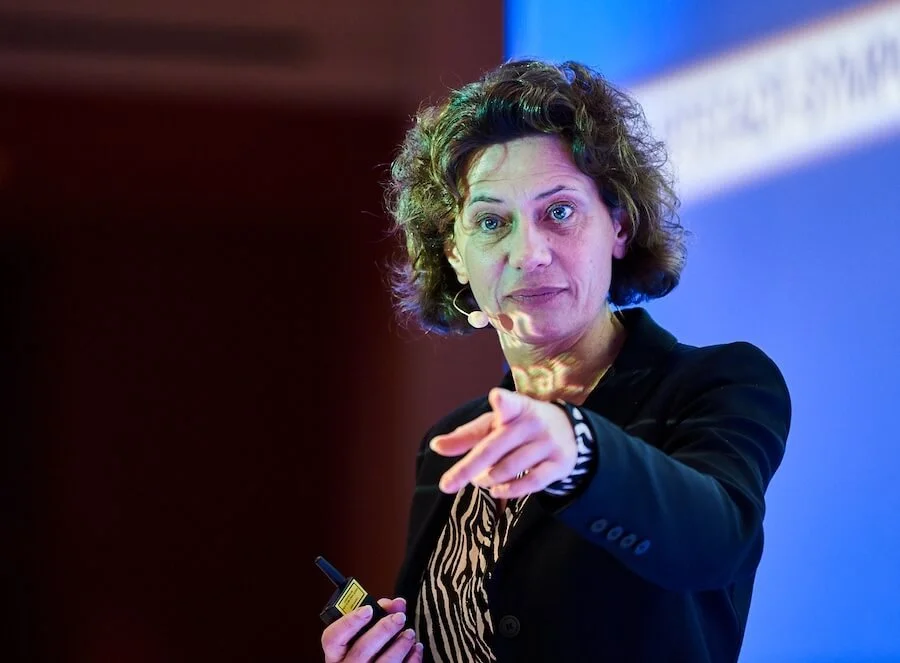 Andrea Belliger spricht auf einer Bühne und zeigt in die Kamera.