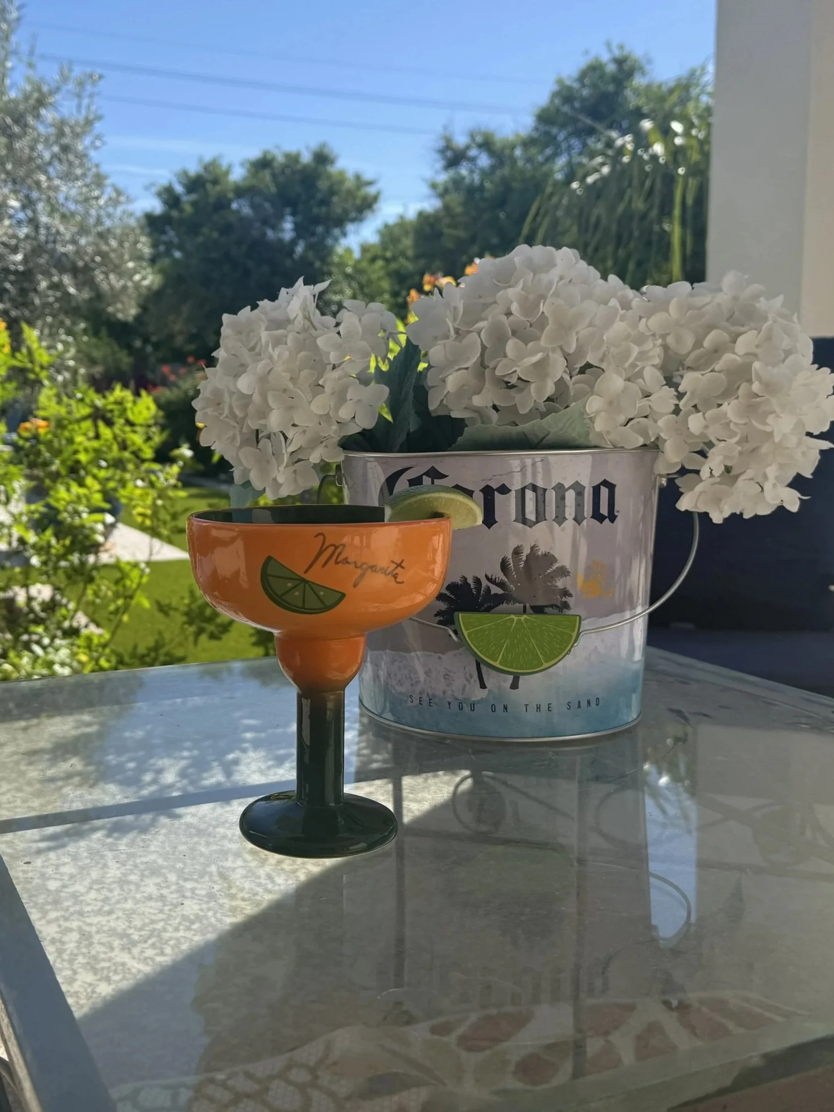 An orange margarita glass with lime garnish next to a bucket of white hydrangeas