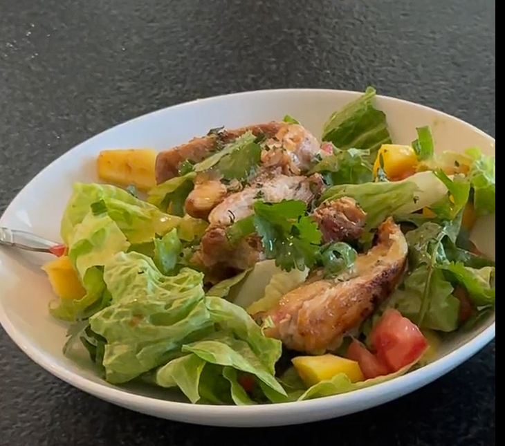 "Mango Chicken Salad with grilled chicken, mango, and greens in a white bowl
