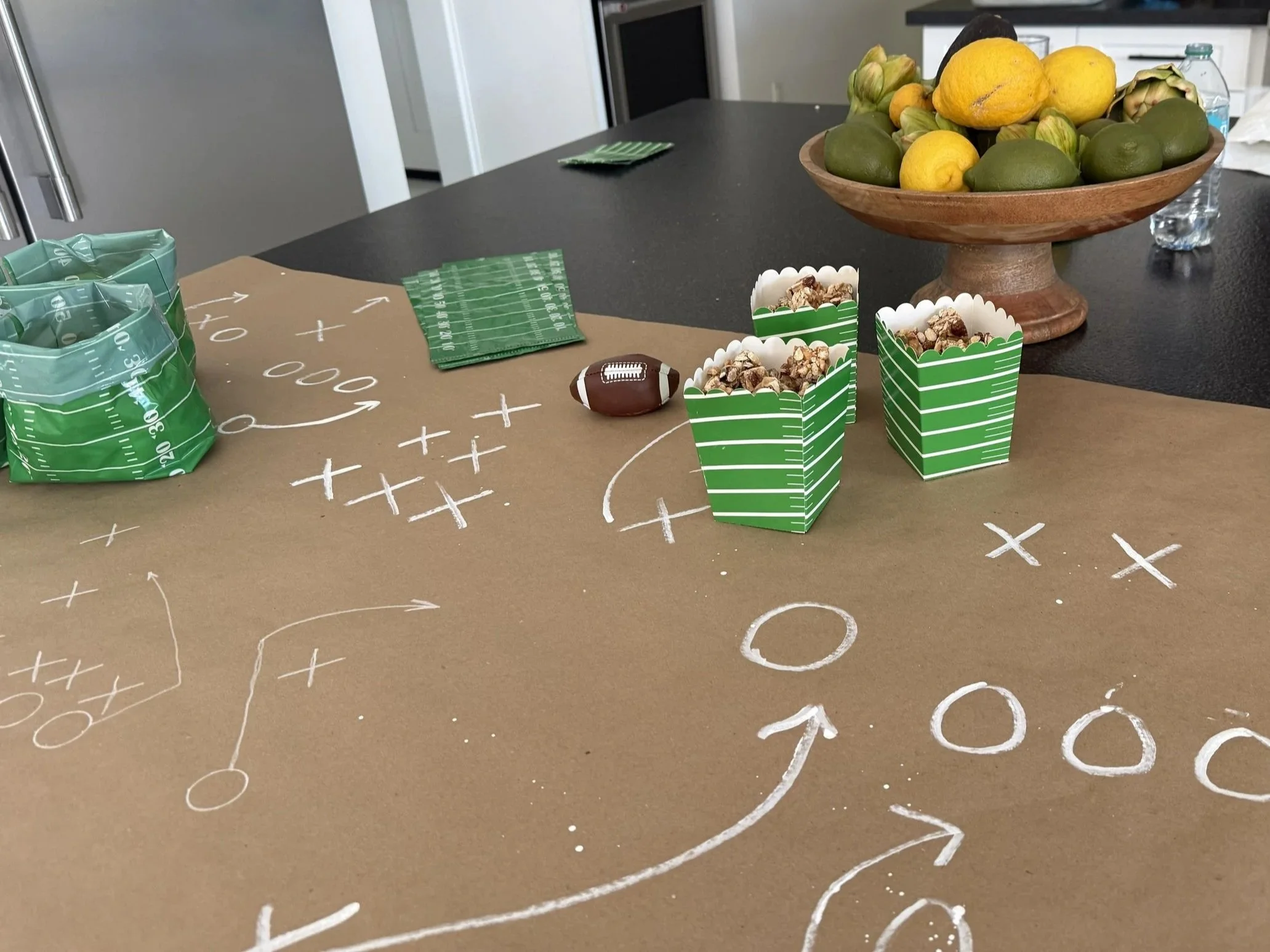 Kraft-paper football field table runner with green striped snack boxes and football-themed decorations.