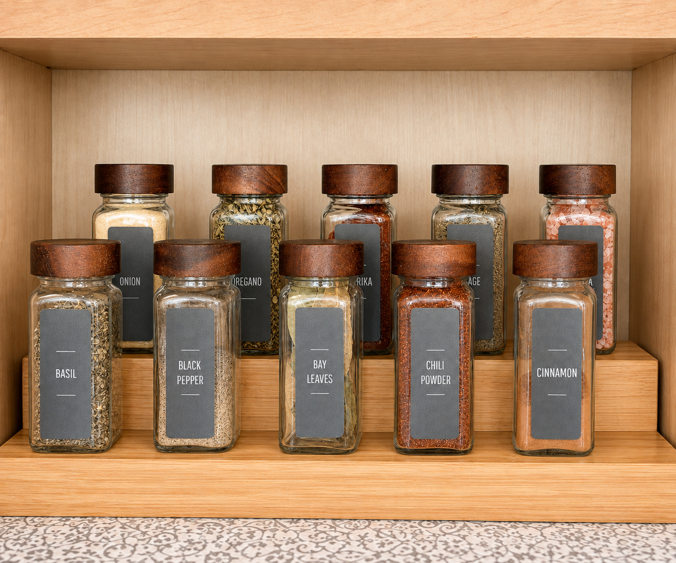 A wooden pantry shelf lined with ten glass spice jars, each with a matching dark green label, organized in two neat rows.
