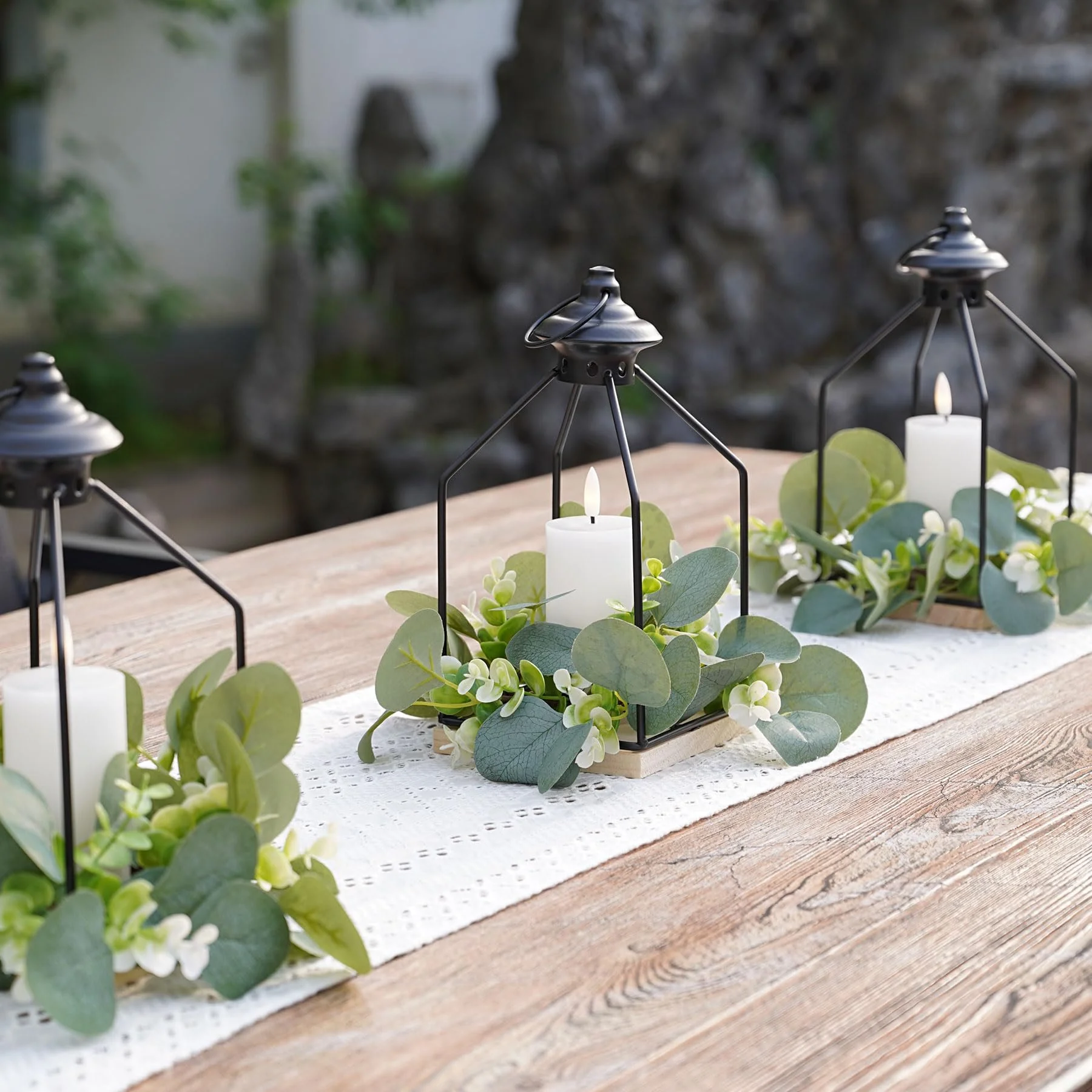 Outdoor table decorated with a black lantern, white candle, and eucalyptus greenery