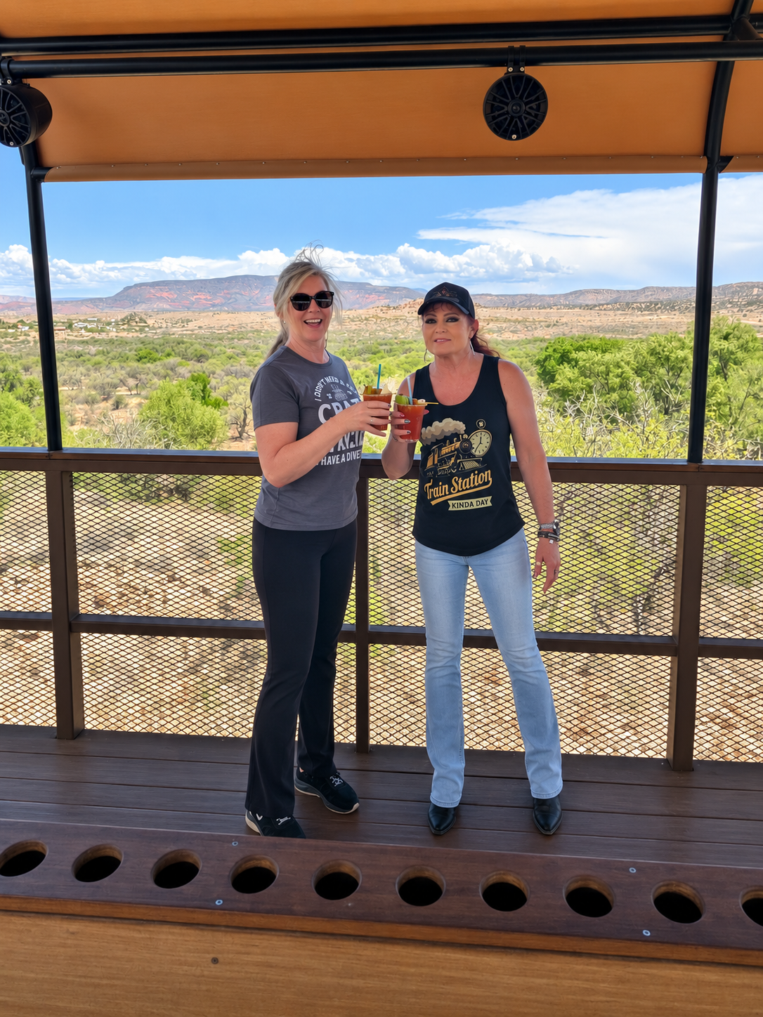 Two friends holding Bloody Marys in the open-air viewing car of the Verde Canyon Railroad.