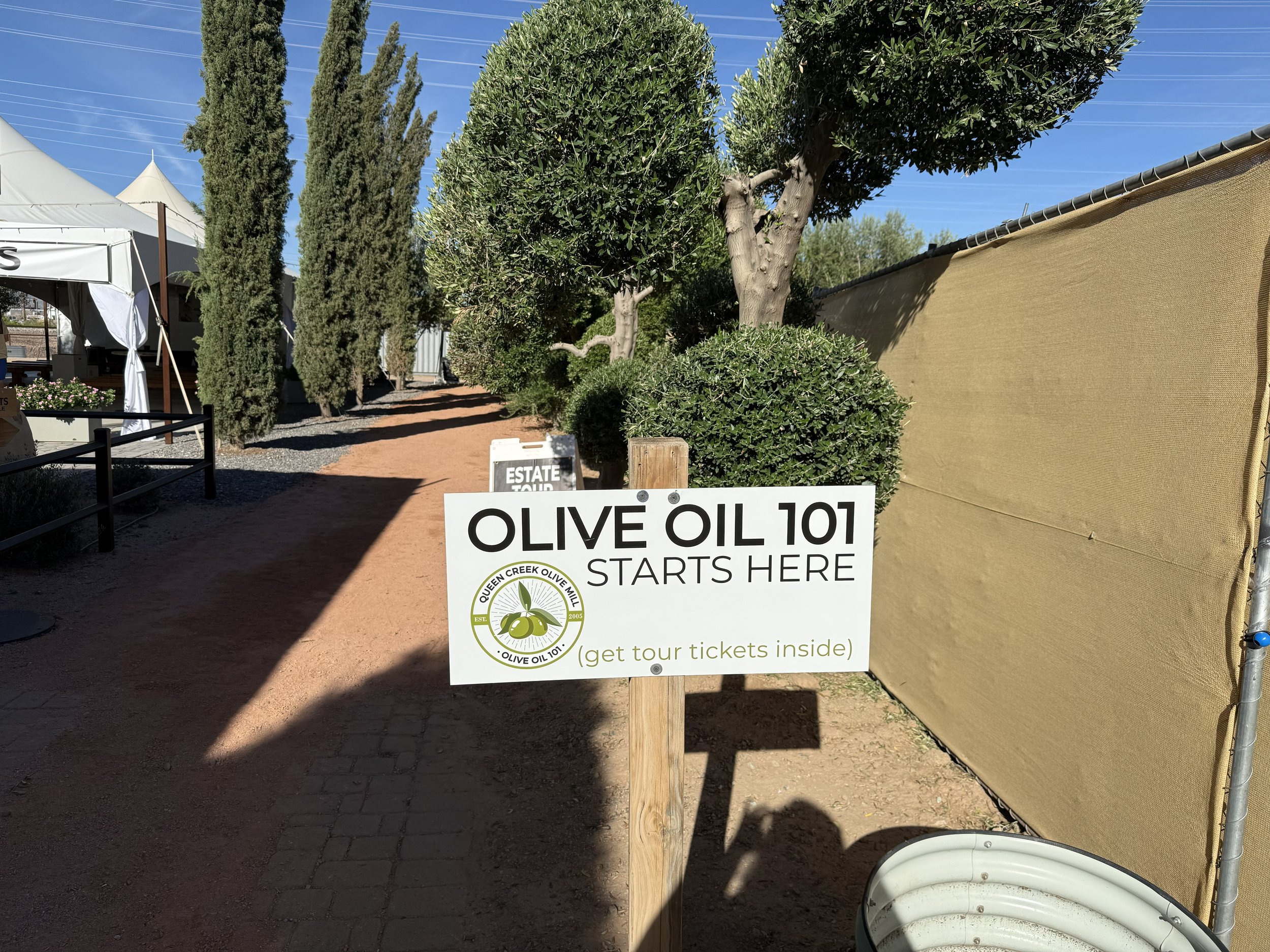 Olive Oil 101 sign beside a tree-lined path at Queen Creek Olive Mill.