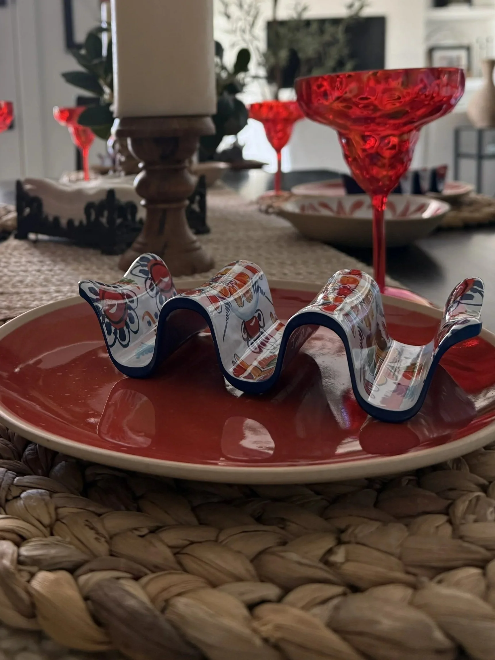 Patterned taco holder on a red plate, styled with red margarita glasses and a candle