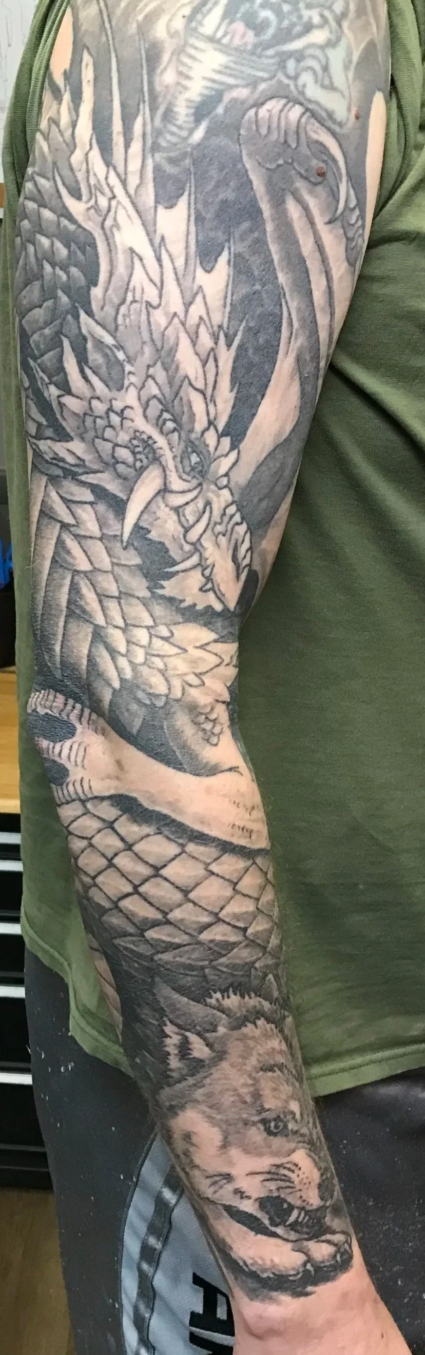 A tattoo sleeve featuring a detailed design of a dragon, a snake, and a wolf, all in black and gray ink.
