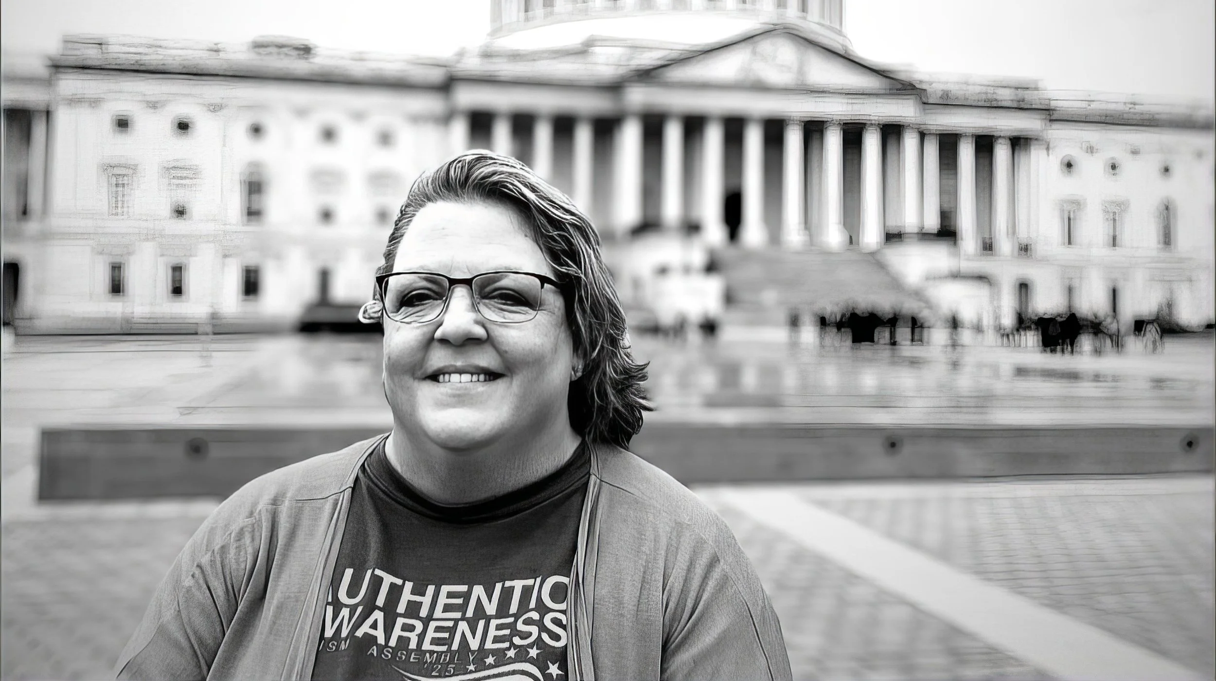 An NCSA caregiver advocate smiling in front of the U.S. Capitol, wearing an Authentic Awareness shirt, calling families to add their voice for severe and profound autism policy